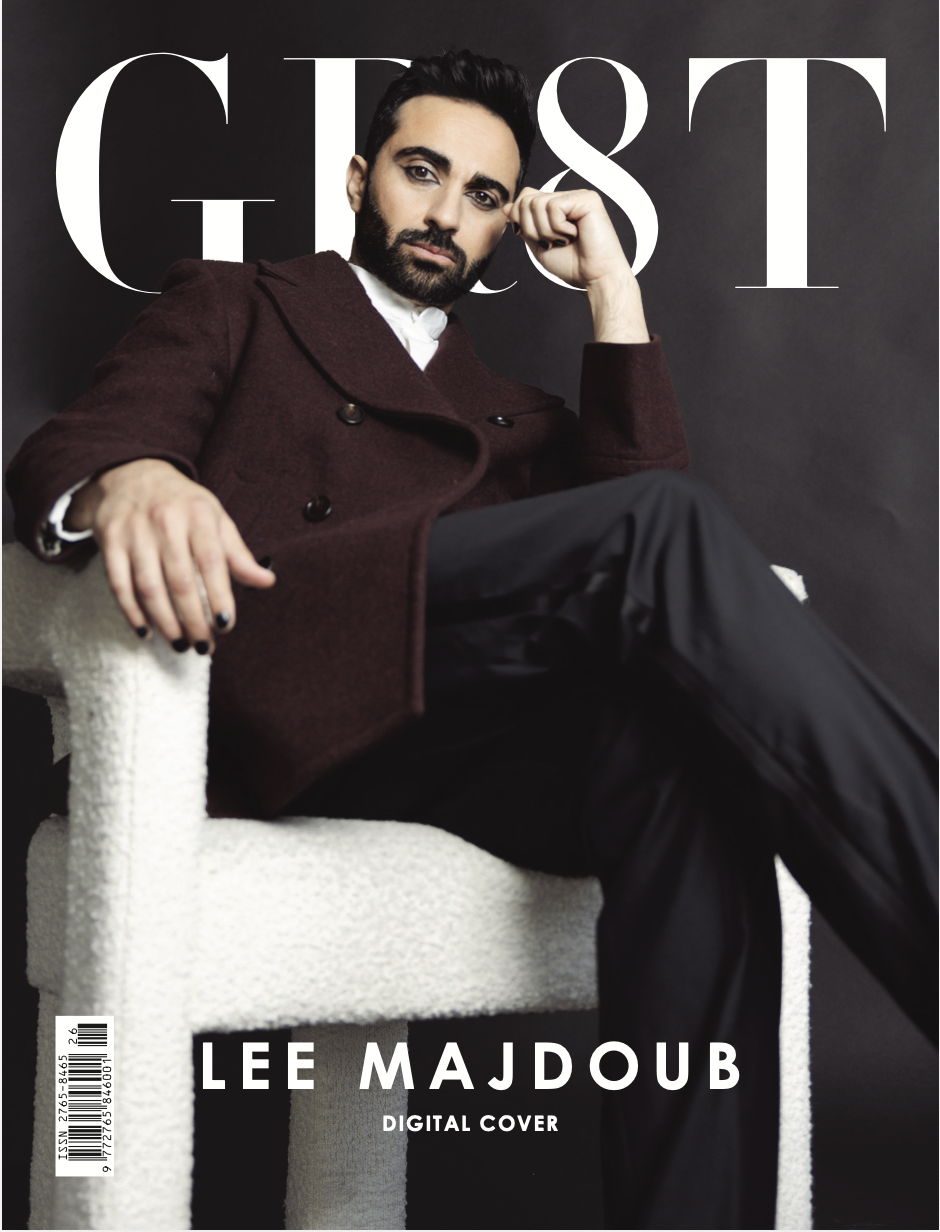 Magazine cover featuring Lee Majdoub sitting in a modern white chair, wearing a dark red coat and black pants, with a dark background and the word 'GUEST' in large white letters behind him.