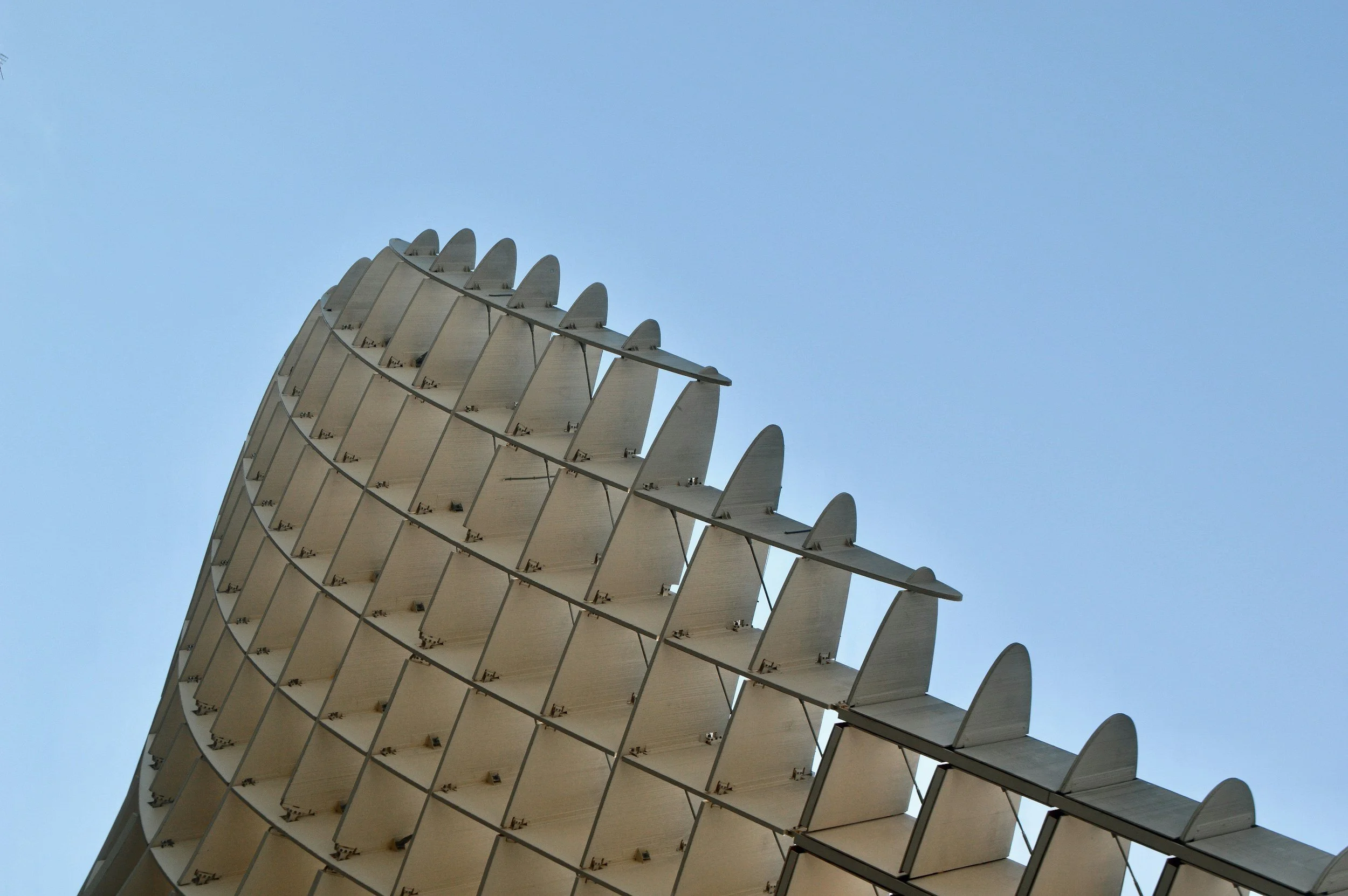 Close-up of a modern architectural building with a curved, sail-like design against a clear blue sky.