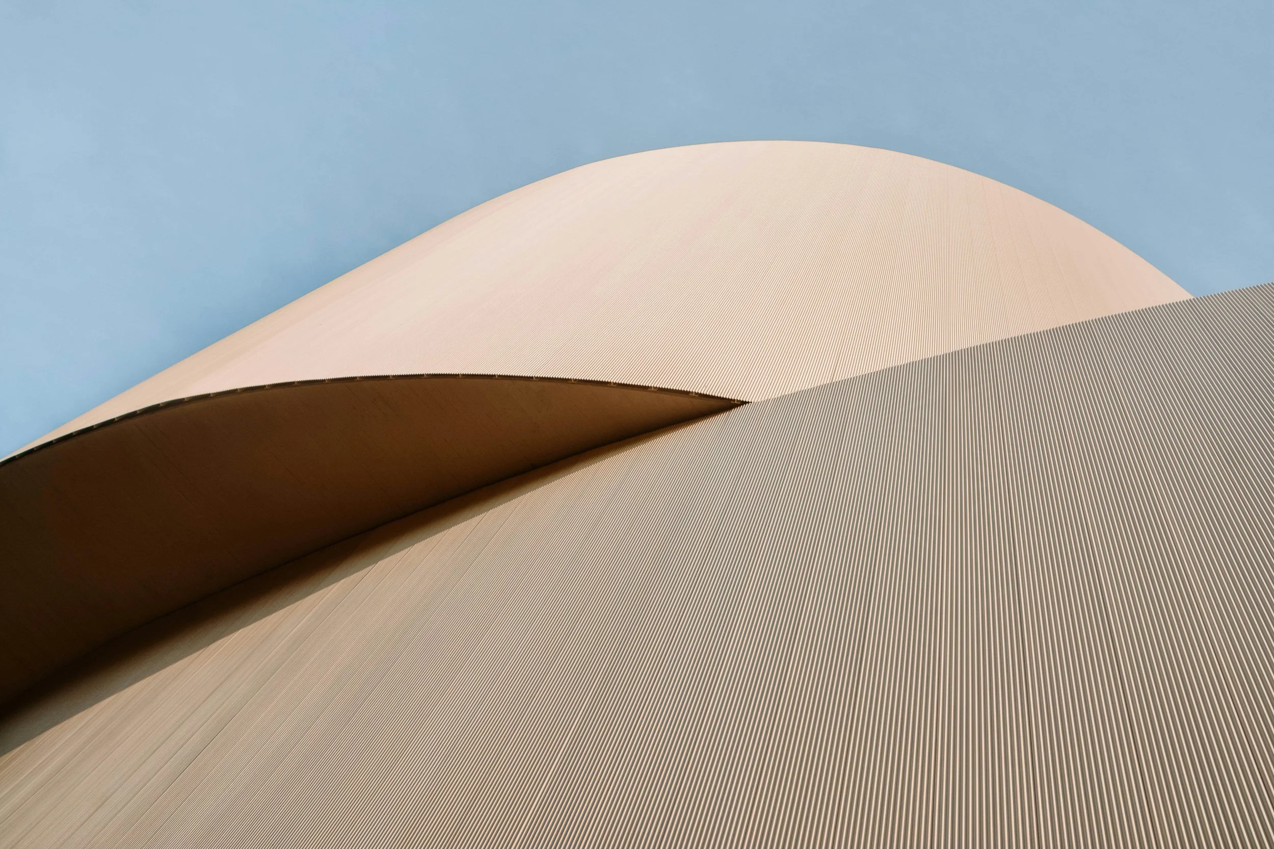 Close-up of a modern architectural building with curving, metallic surfaces and a blue sky background.