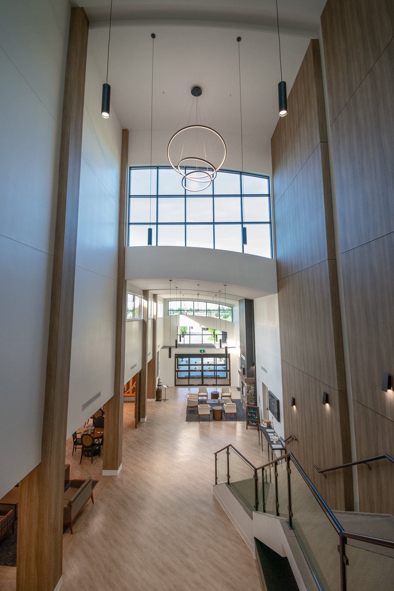 Interior view of a modern, spacious lobby with tall ceilings, large windows, and minimalist furniture, including chairs and tables, with wood and white decor.