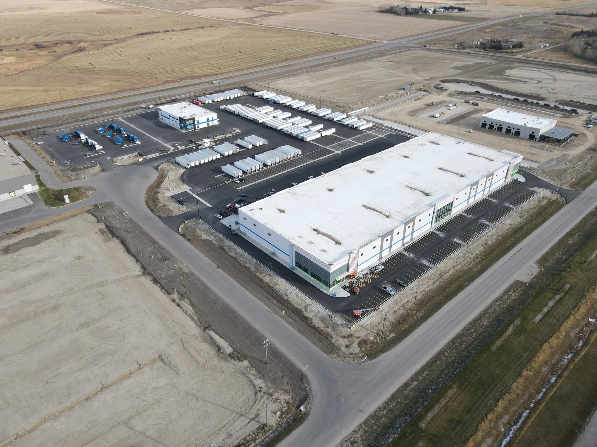 Aerial view of a new, large commercial warehouse with a parking lot and surrounding empty land.