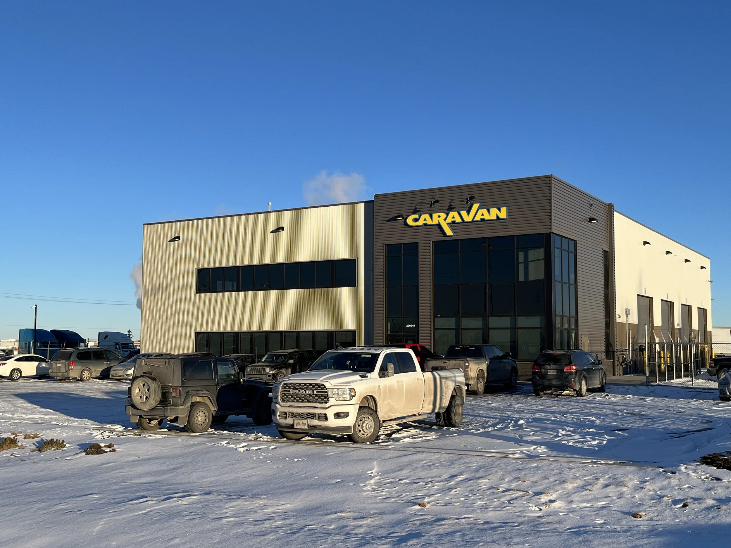 Commercial building with the sign 'Caravan', surrounded by parked trucks and cars on a snowy day.