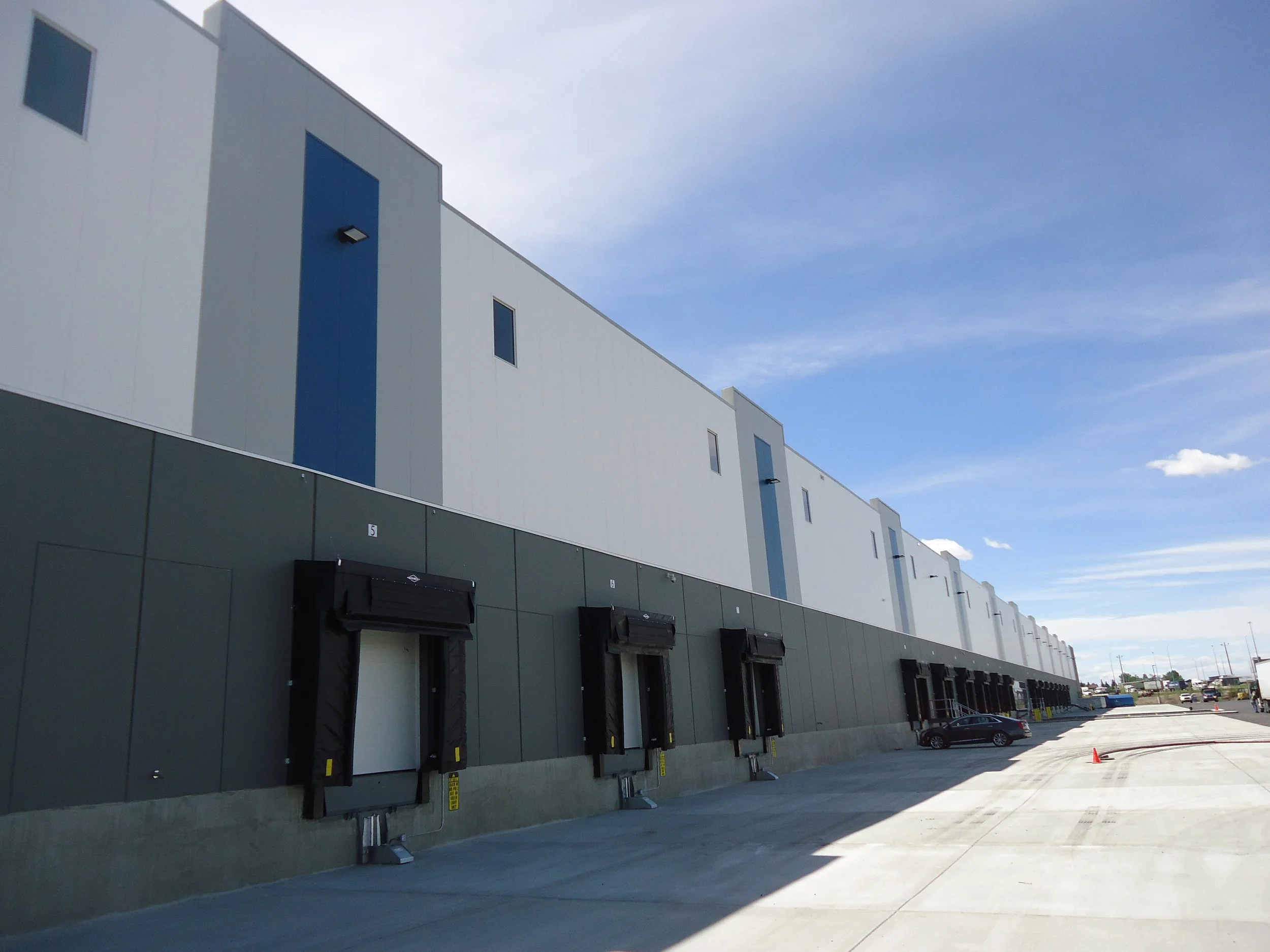 A large industrial warehouse with multiple loading docks and delivery bays under a blue sky.