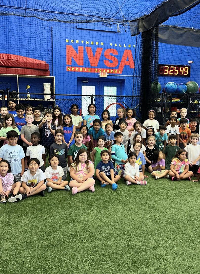 Group of children inside an indoor sports facility at Northern Valley Sports Academy, posing for a photo with a digital clock showing 3:54:49 in the background.