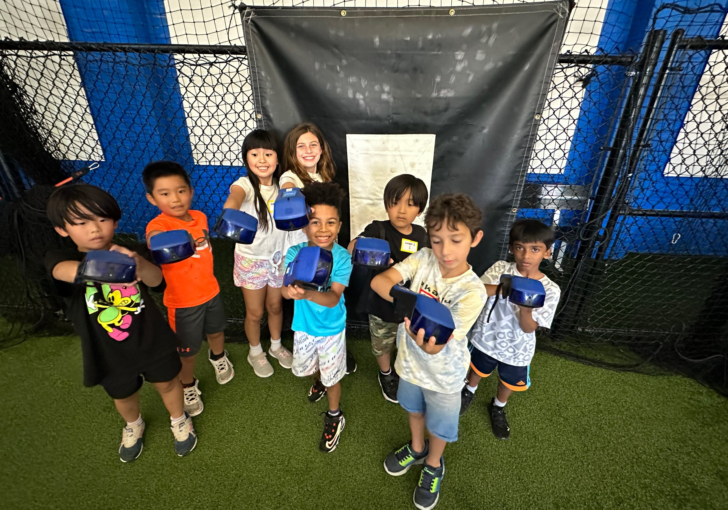 Group of young children holding blue laser tag guns at an indoor laser tag arena with black netting and blue and white walls.