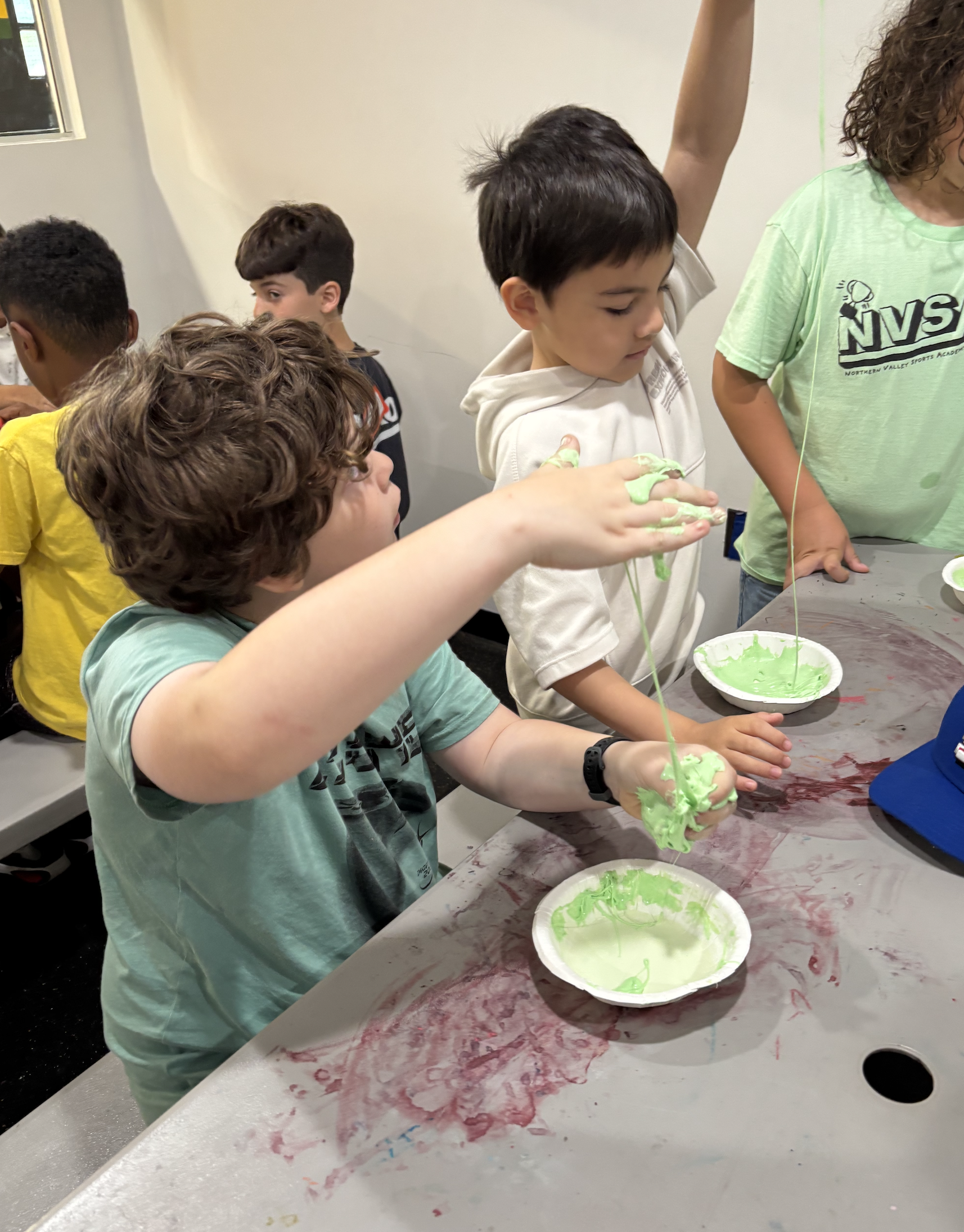 Children at a table playing with green slime in bowls.