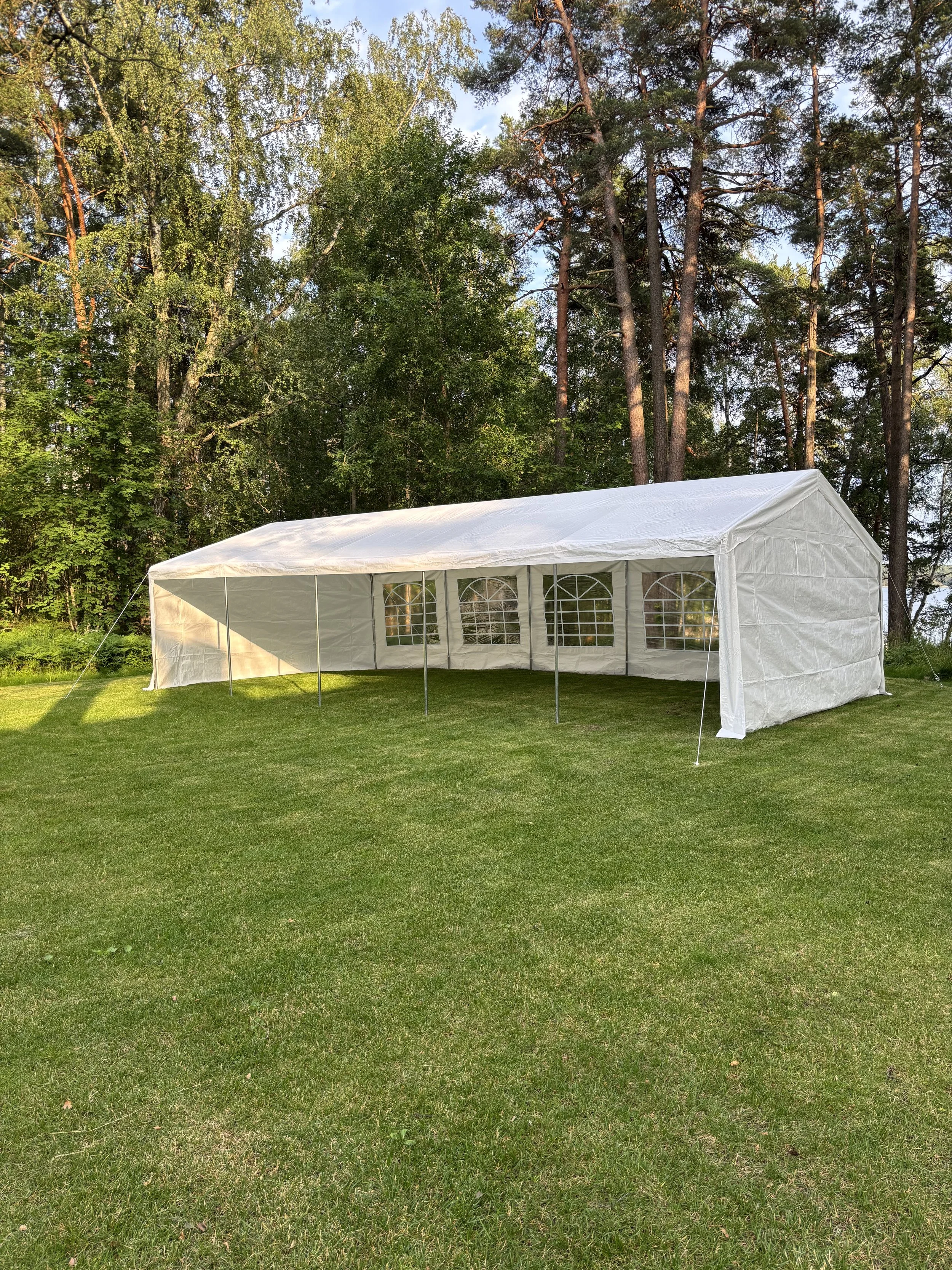 Valkoinen juhlateltta nurmikkoalueella ja taustalla puita ja taivasta.