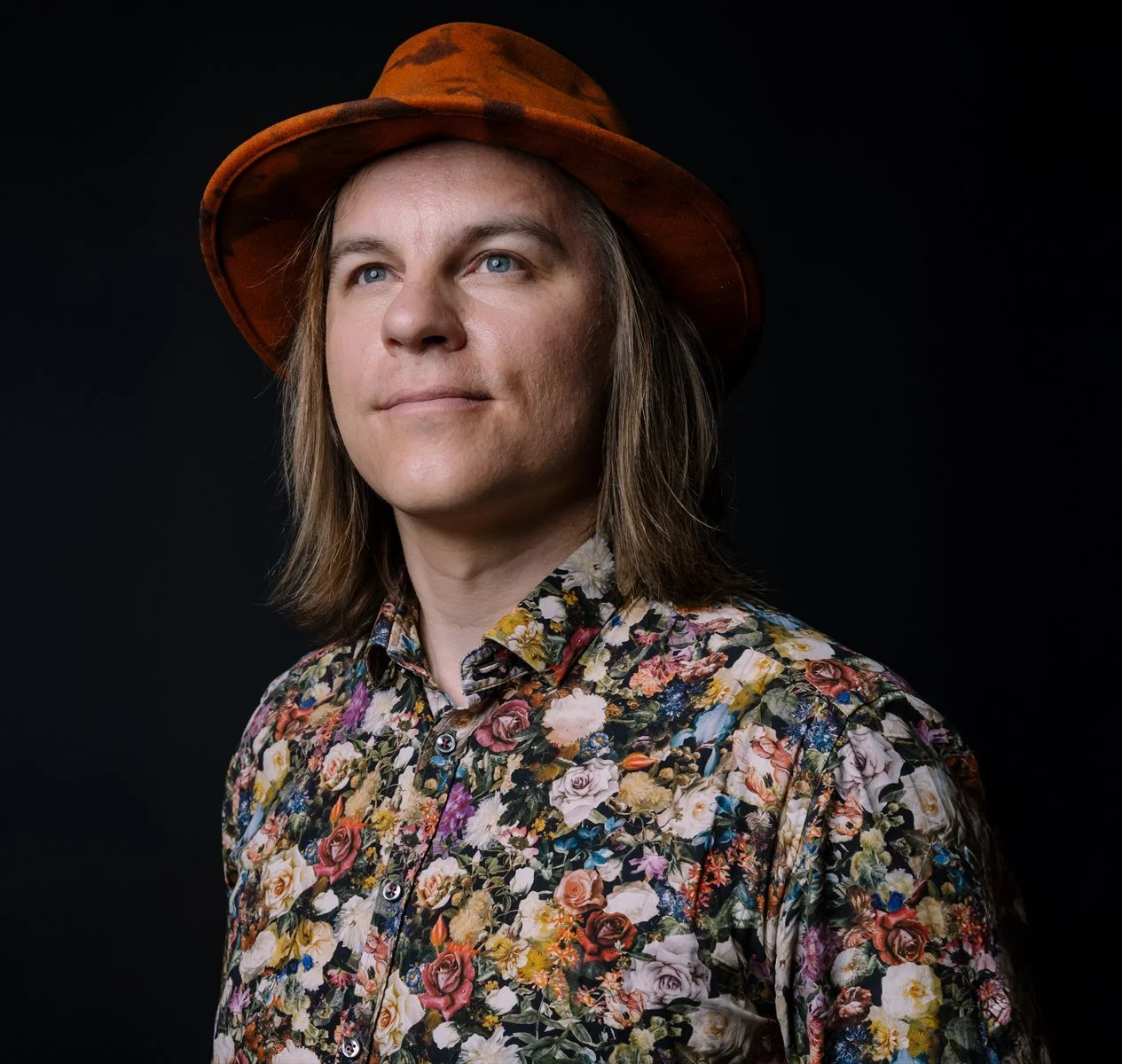 Frank kukkakauluspaidassa ja hatussa mustalla taustalla.