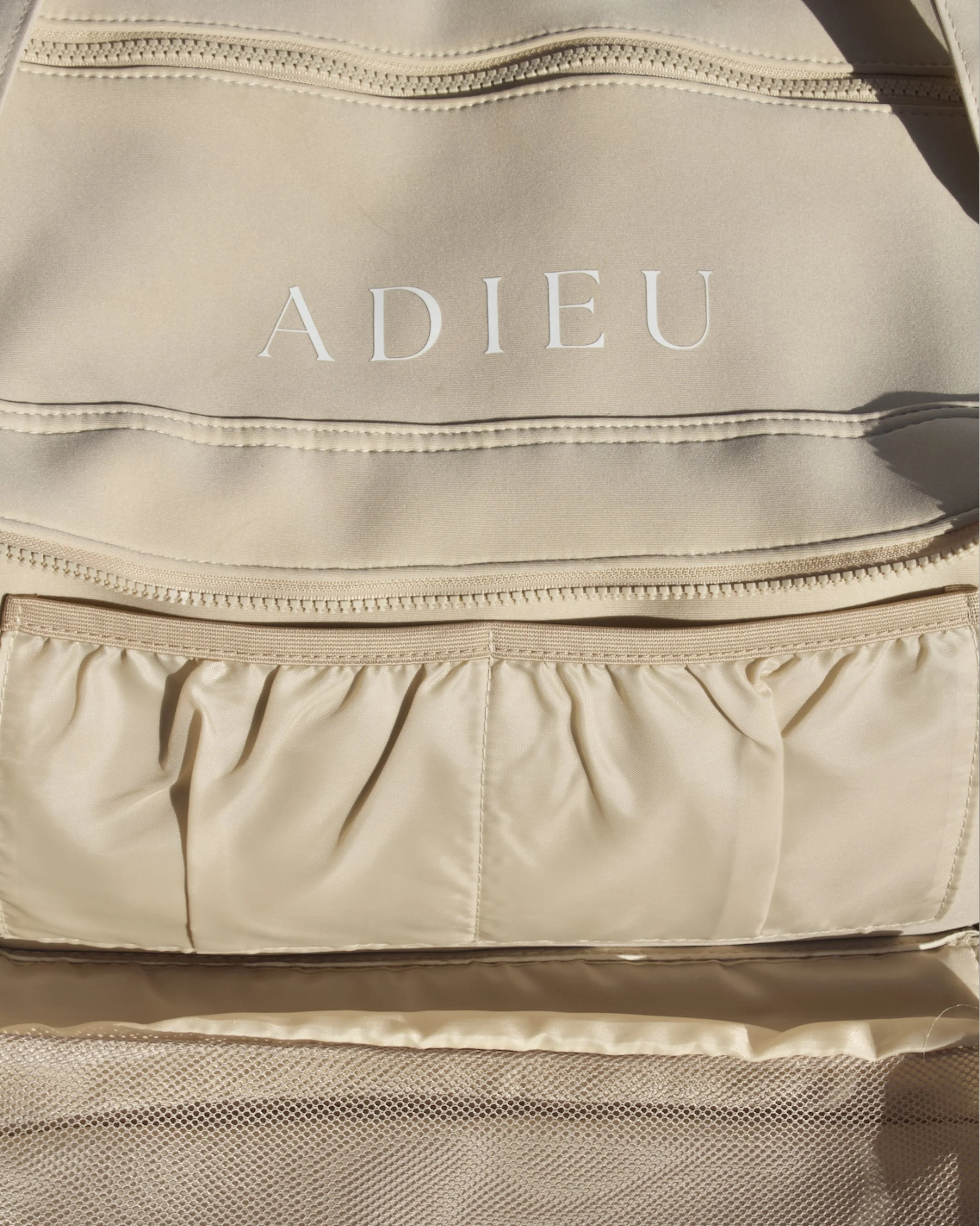 Close-up of the ADIEU logo and slip pockets with elastic organisational pocket on the Core Duffle weekender bag.
