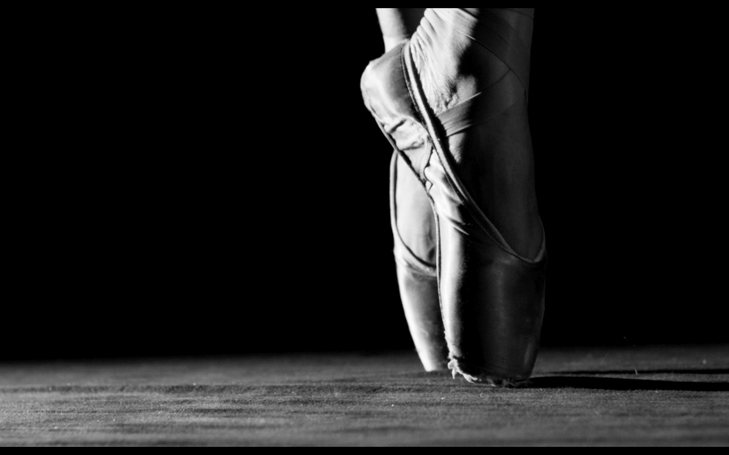Close-up of a ballet dancer's feet in pointe shoes, standing on tiptoe on a wooden floor in black and white.