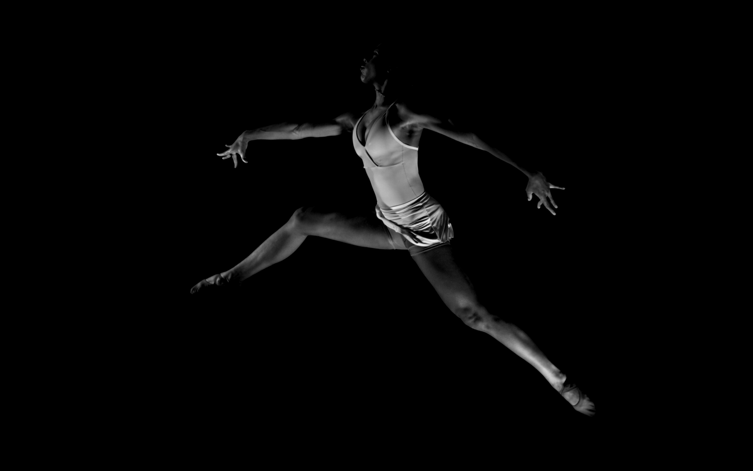 A dancer in a leotard performing a leap against a black background.