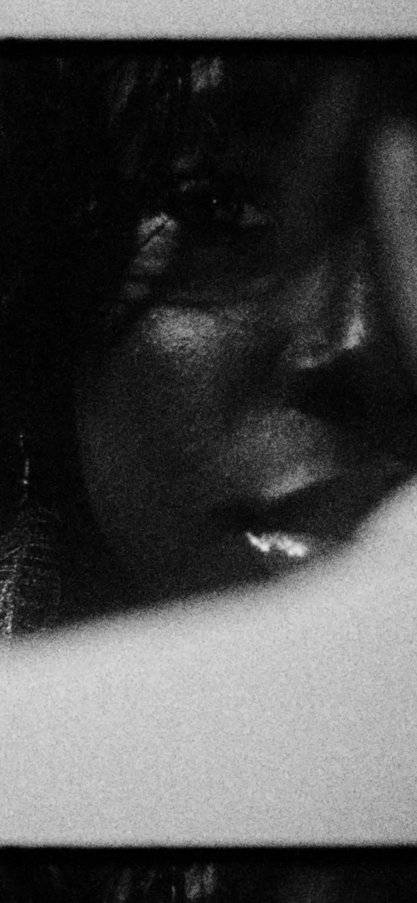 A close-up, black-and-white photo of a woman's face with her eyes closed and lips slightly parted, resting her chin on her hand.