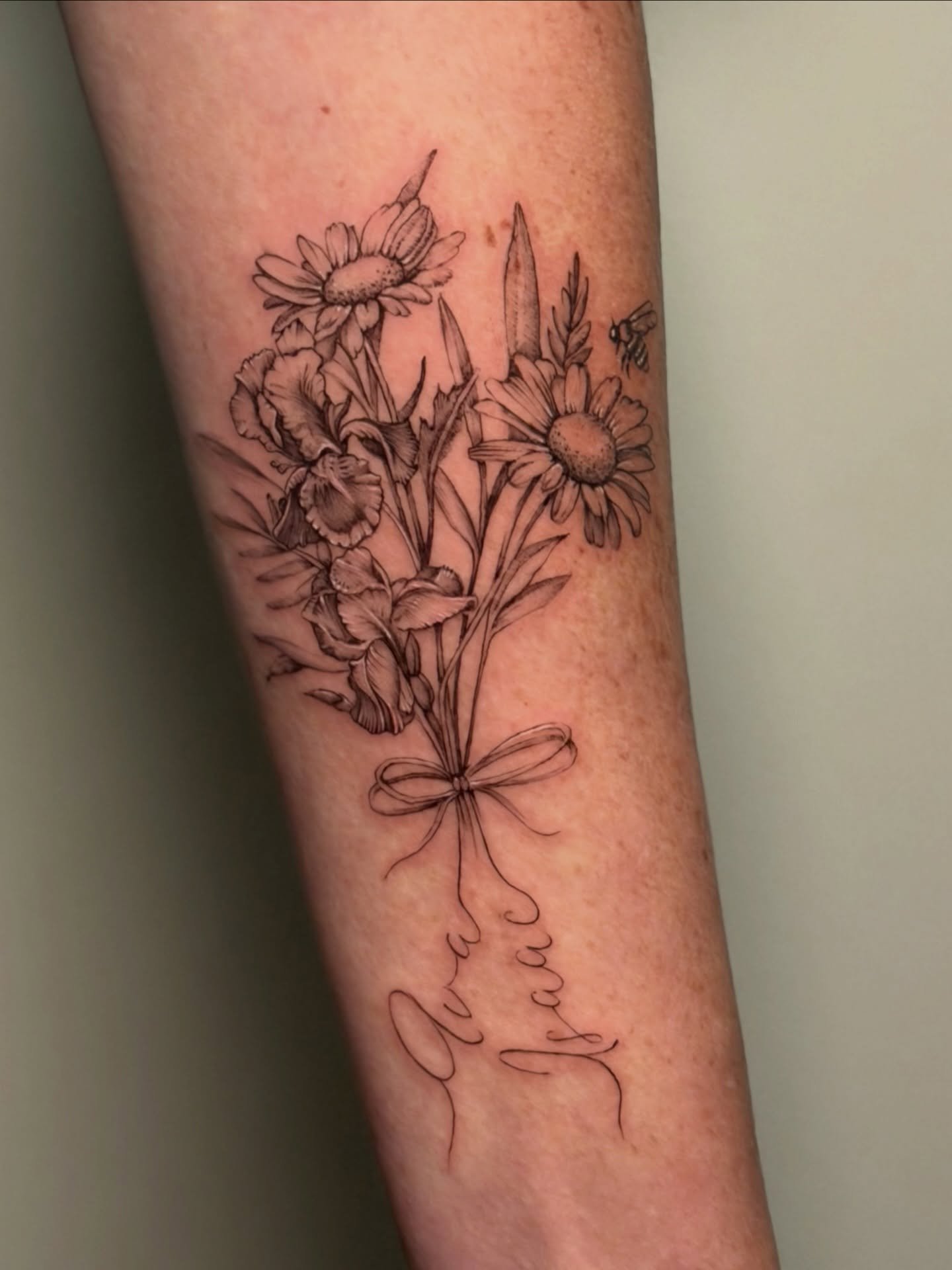 Elegant fine-line bouquet tattoo ✨
Hand-tied irises and daisies finished with a delicate bow and custom script. 

Clean, timeless, and perfectly placed on the arm. Precision and detail in every petal.

#finelinetattoos #westpalm #palmbeachstyle #sout