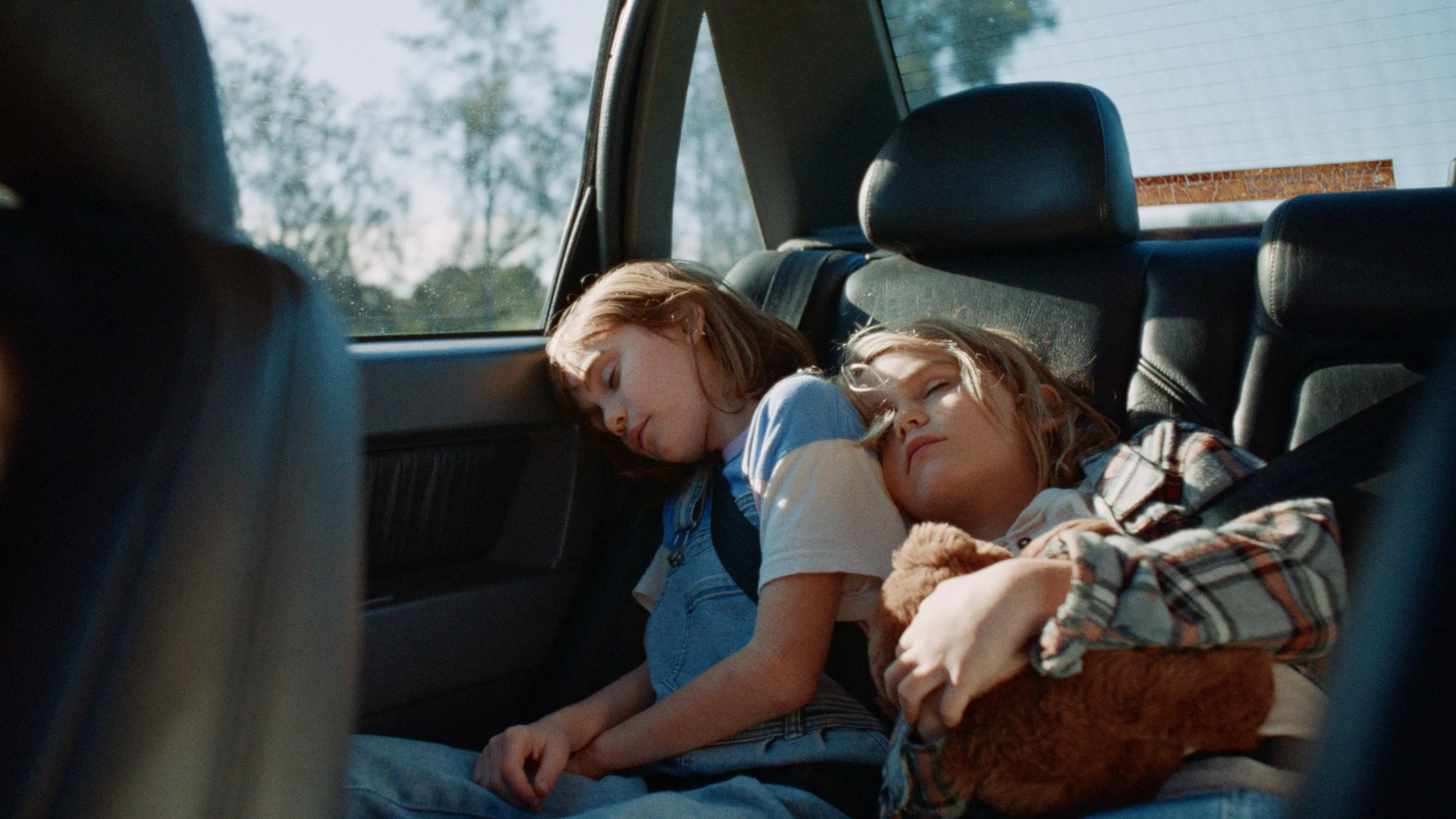 Two children dreaming in the backseat of an old car.