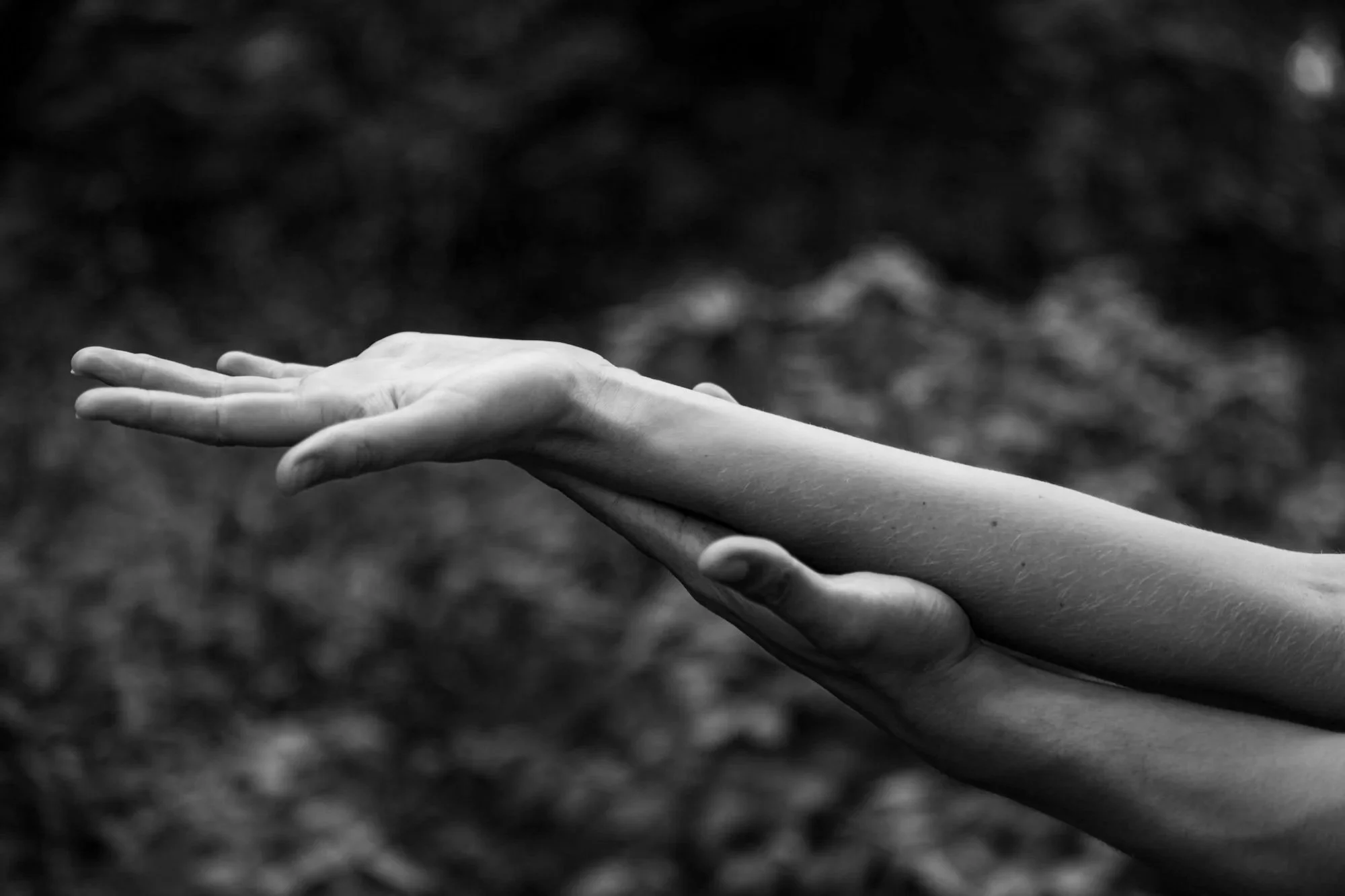 Black and white photo of a person laying their arm and hand flat, with fingers extended, against a blurred natural background.