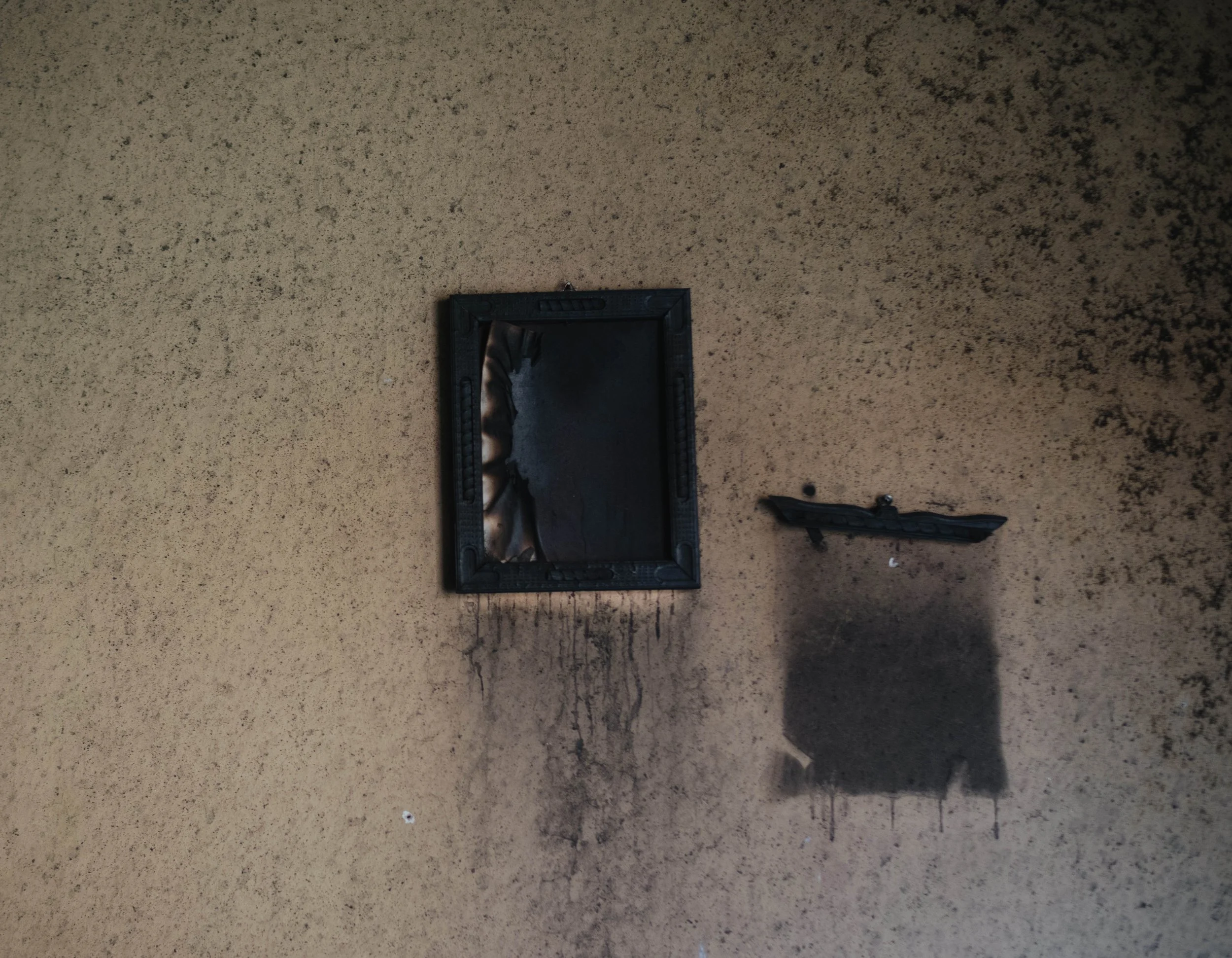 A charred picture frame hangs on a soot-stained wall inside a damaged space in Aguililla, Michoacán.