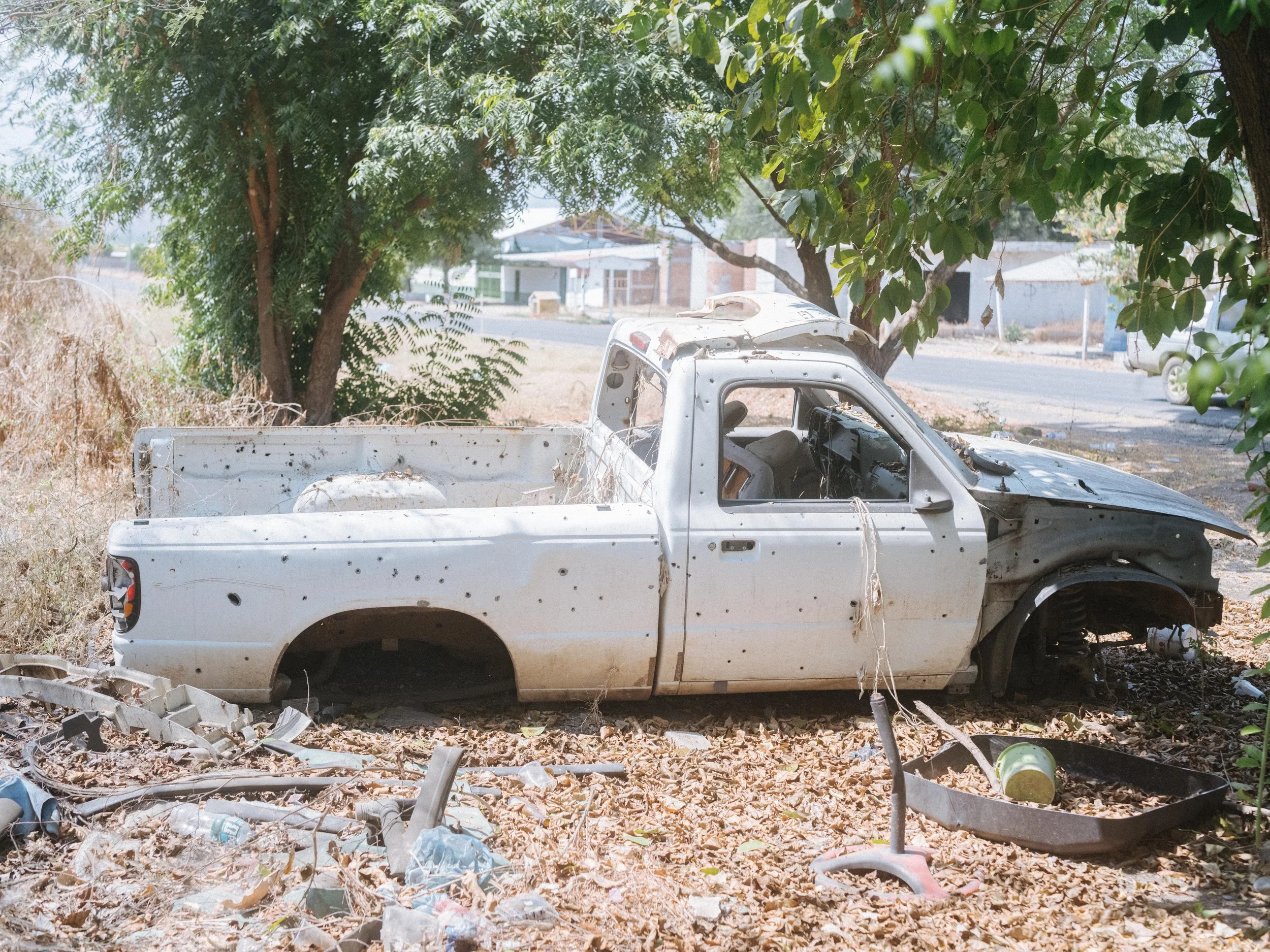 An abandoned pickup truck riddled with bullet holes sits along a road near Aguililla, Michoacán, an area marked by years of cartel violence and armed confrontations.