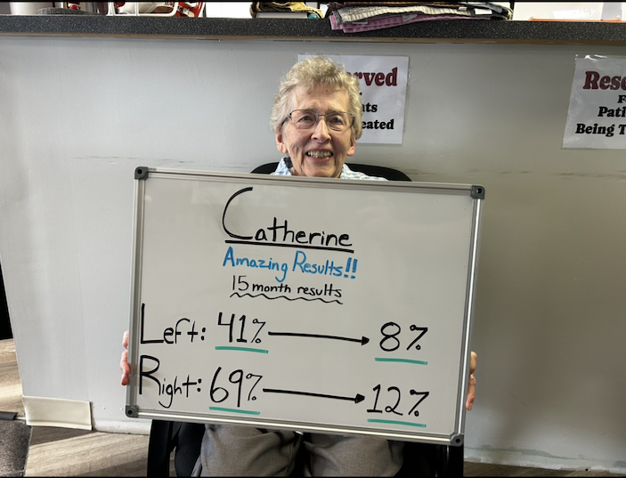 Elderly woman smiling while holding a whiteboard showing health improvement results over 15 months.