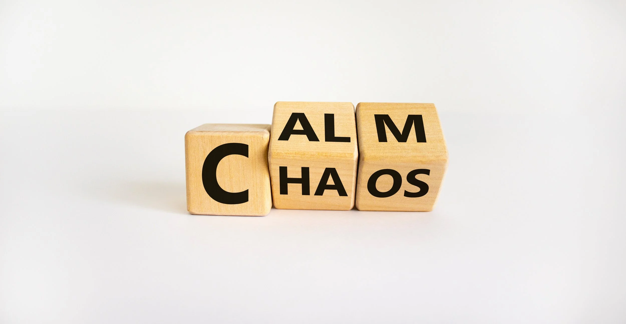 Wooden blocks arranged to spell 'CHAOS' with 'ALM' above, set against a plain white background.