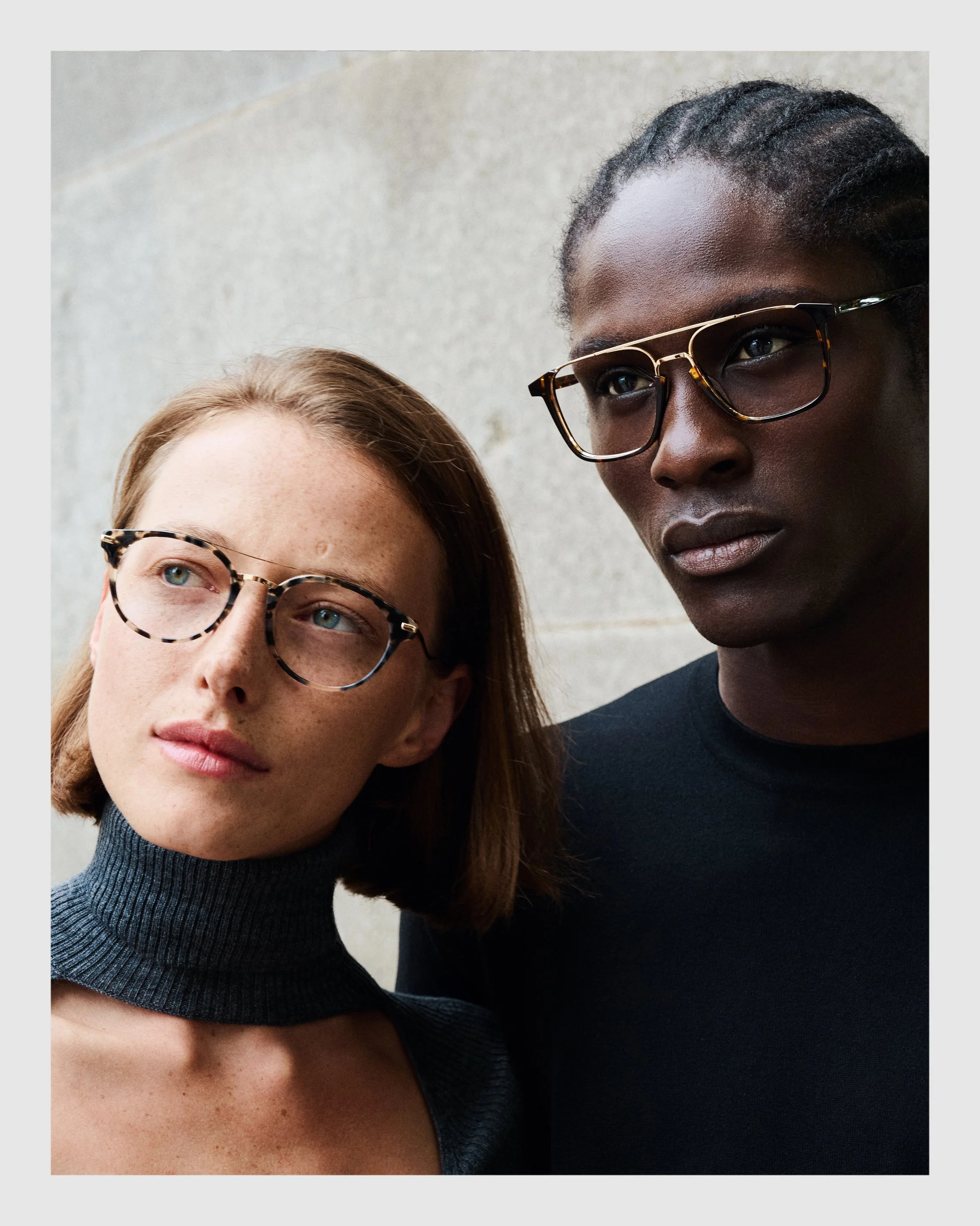 Close-up portrait of a female and male model wearing William Morris optical glasses against a neutral background.