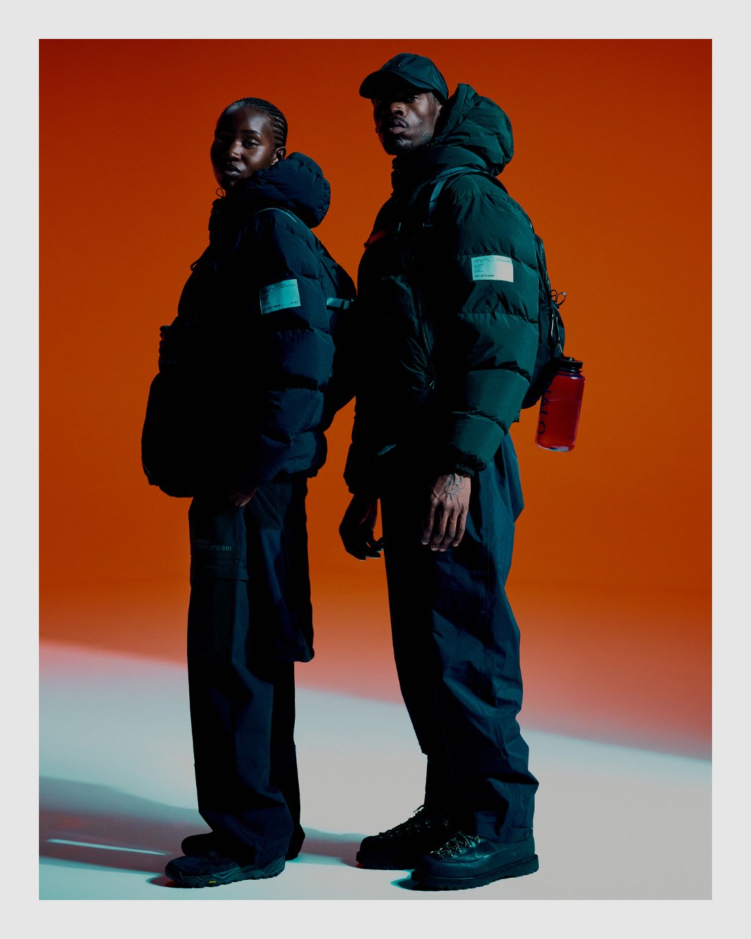 HALO campaign image of two models in technical outerwear against orange studio background