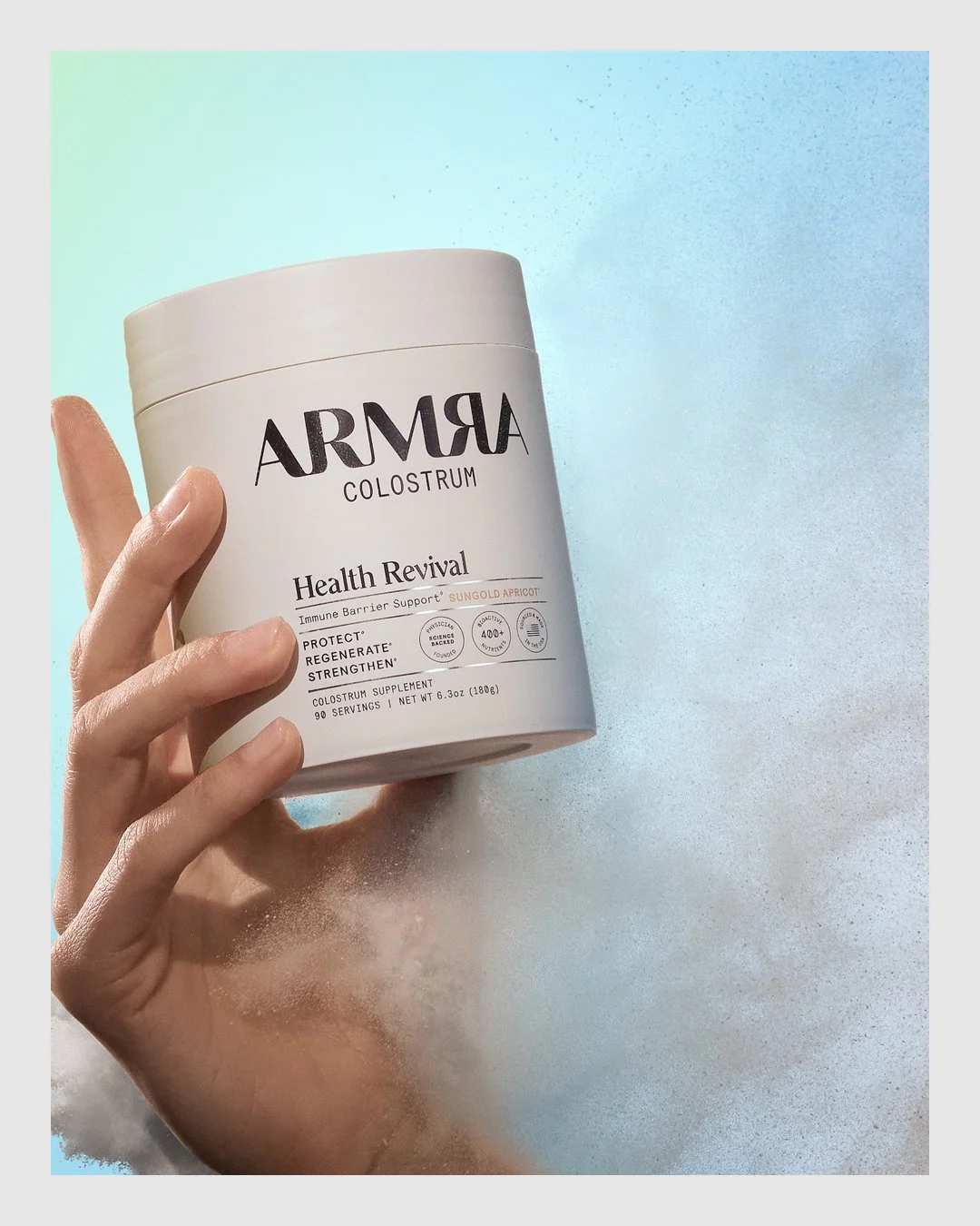 Hand holding ARMRA Health Revival product against a soft blue background