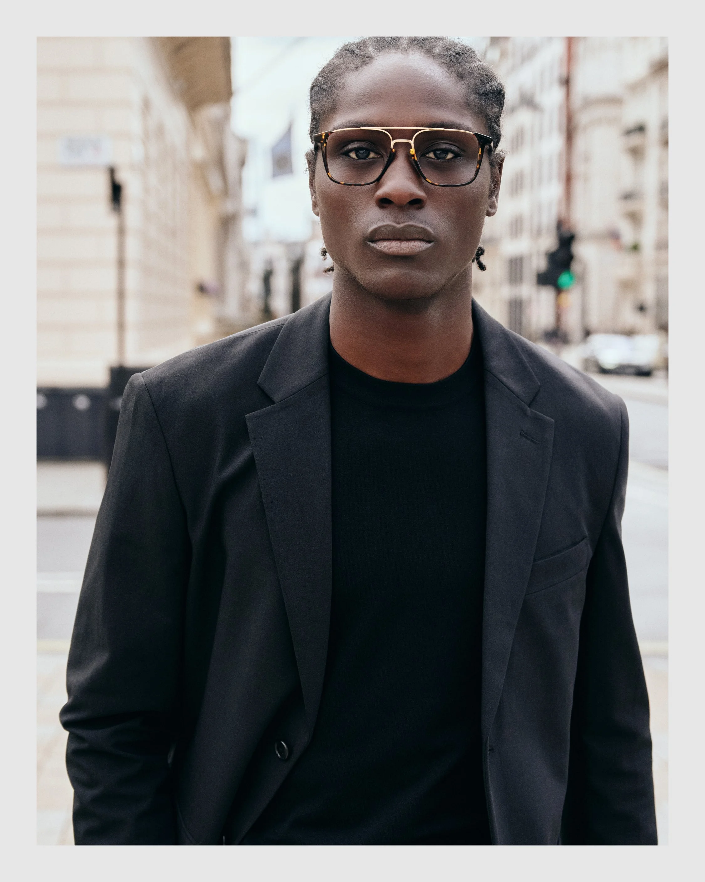 Male model wearing tortoiseshell optical glasses and a black blazer on a London street.