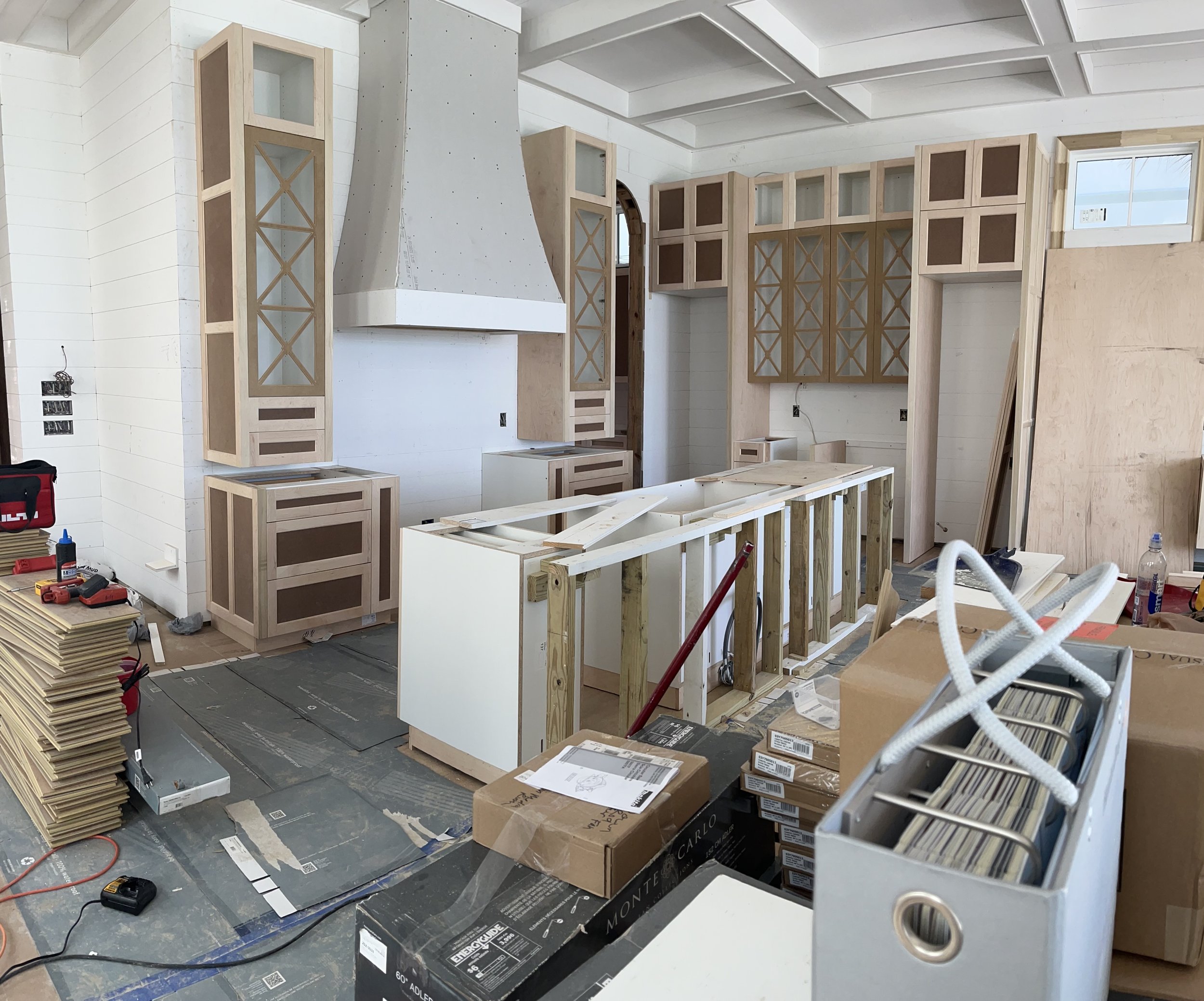 Kitchen under construction with unfinished cabinet installation, stacks of materials, and tools on the floor.