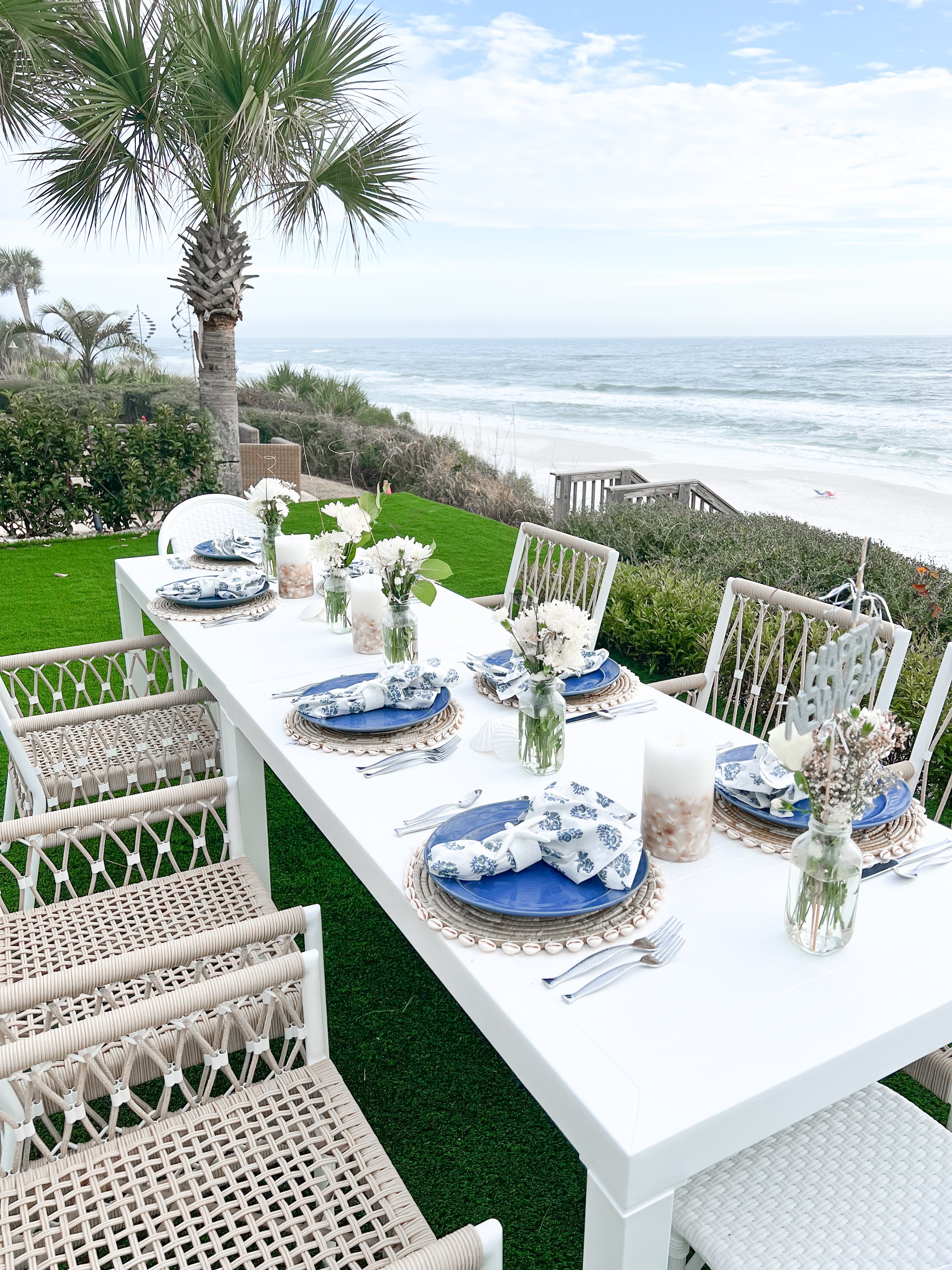 Outdoor dining setup with a white table, wicker chairs, ocean view, and blue and white tableware.