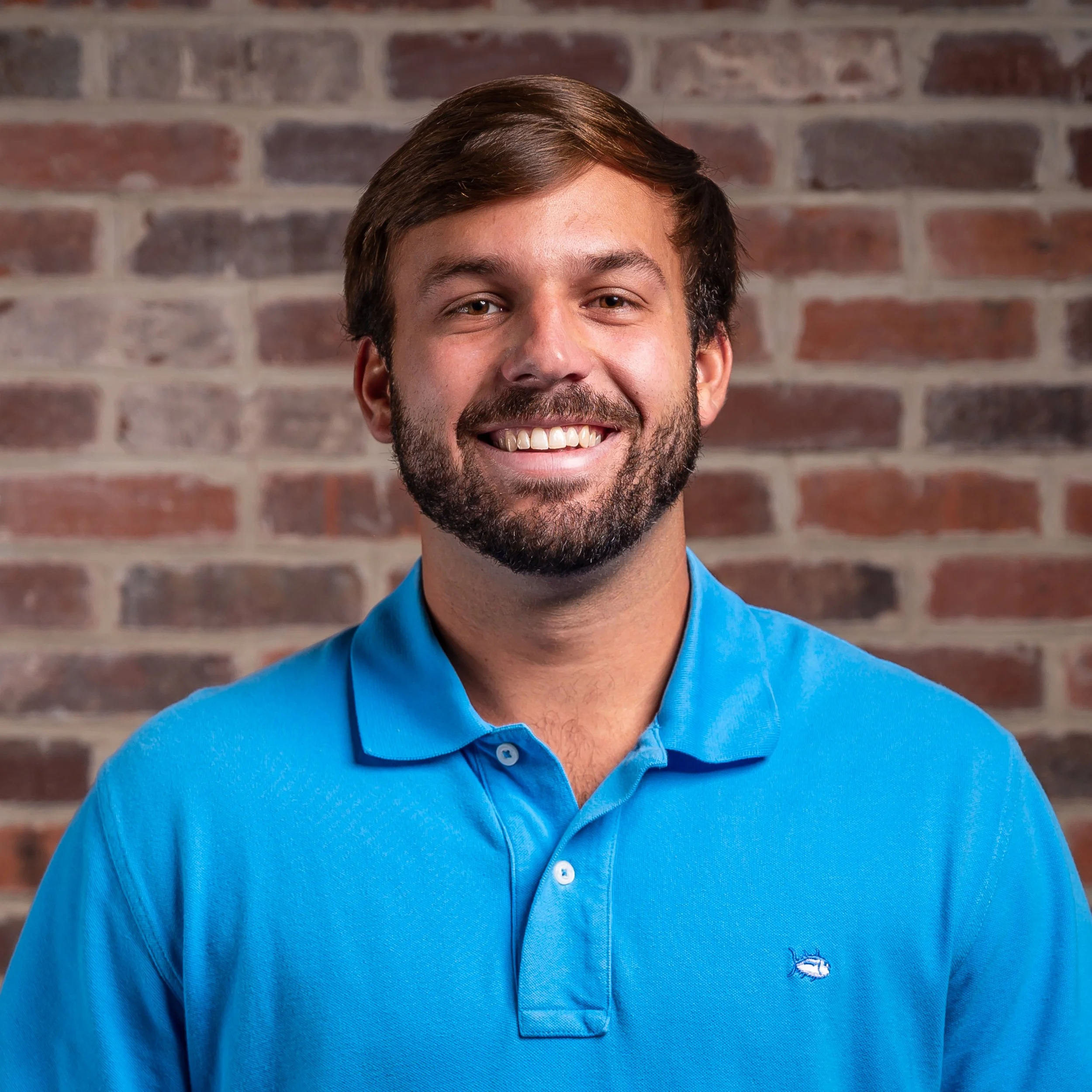 Man with a beard wearing a checkered shirt giving a presentation or speech, with a microphone headset, standing in front of a colorful gradient background.