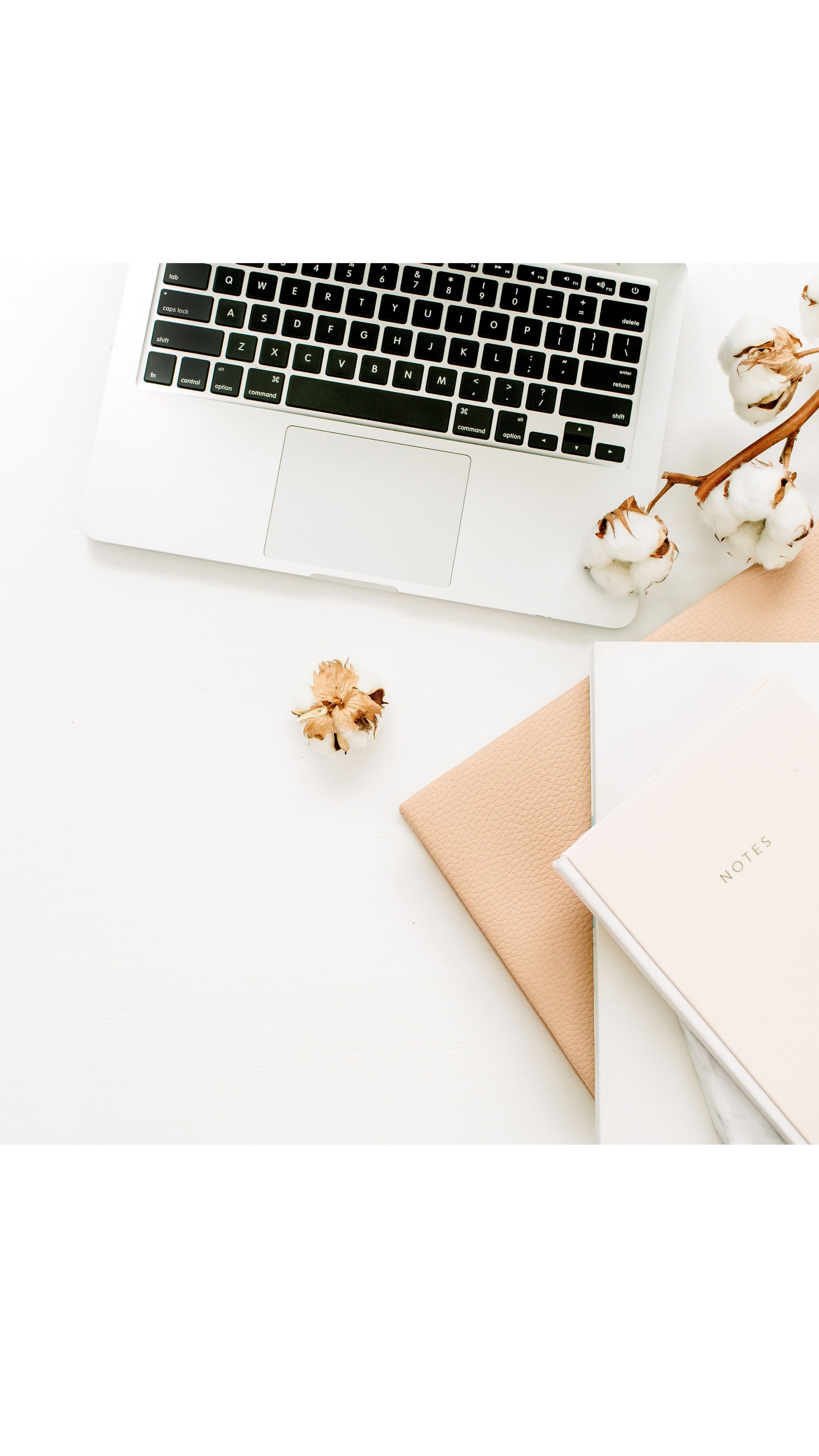 A white desk with a silver laptop, a cotton branch, a beige textured notebook, and a white notebook labeled 'Notes'.