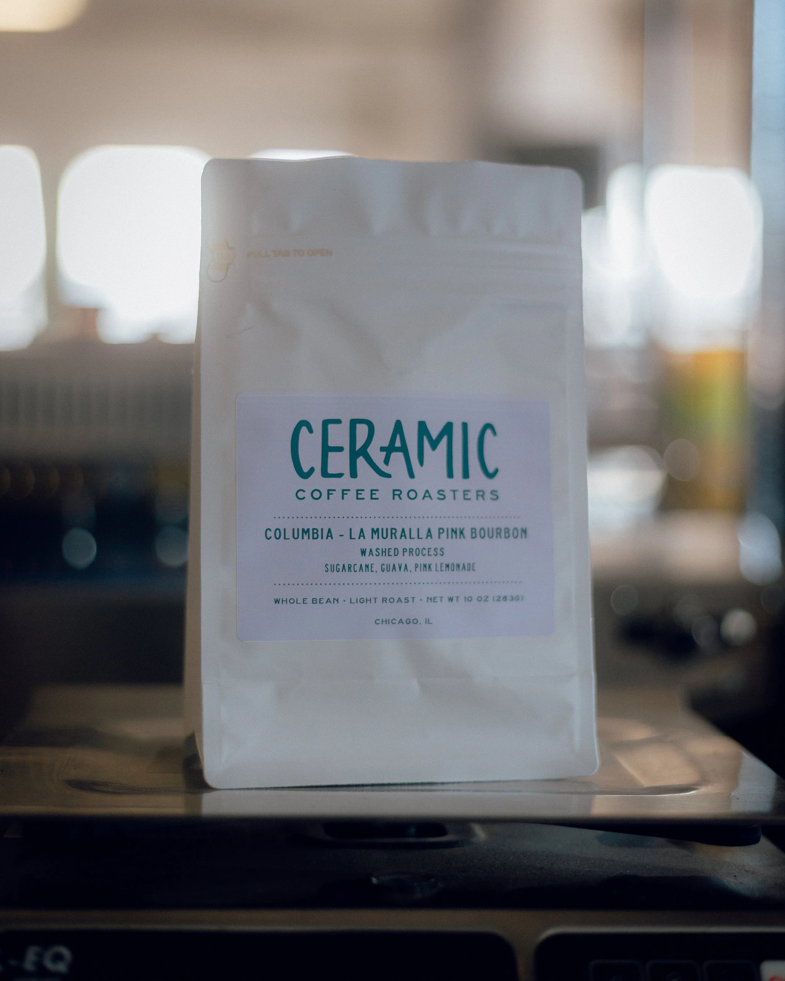 Close-up of a coffee bag labeled Ceramic Coffee Roasters, with flavor notes of Columbia, La Muralla Pink Bourbon, washed process, and ingredients including sugarcane, guava, and pink lemonade, on a wooden surface.