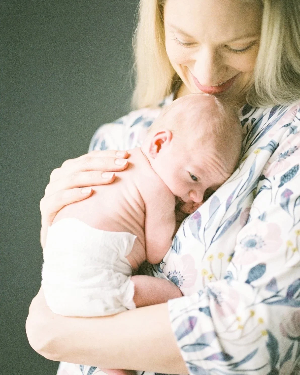 A woman with blonde hair holding a nursing baby close to her chest, with her head gently resting on the baby's head.