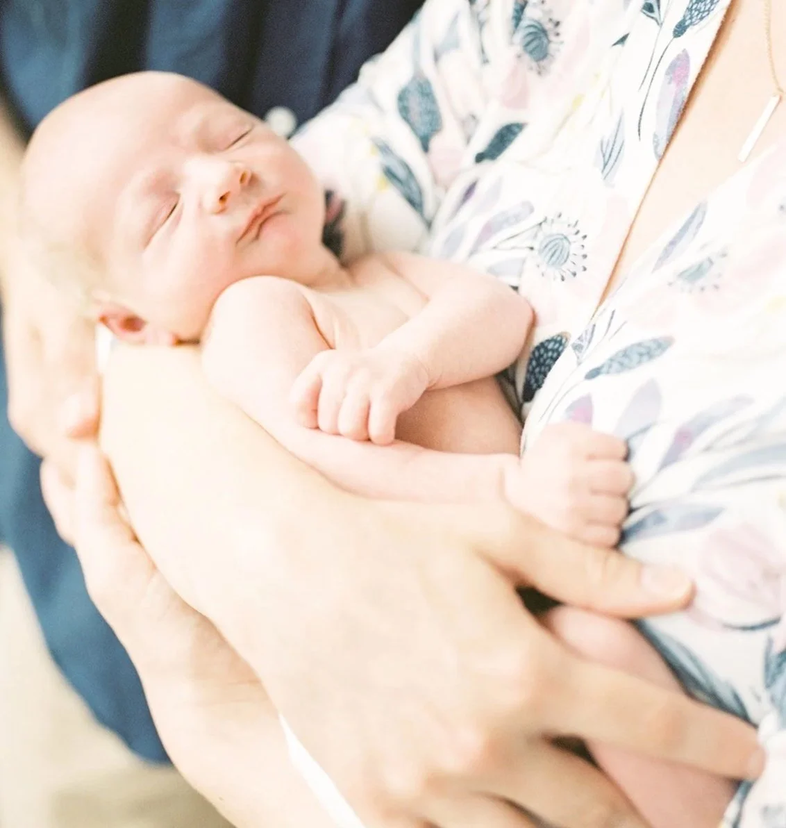 A newborn baby sleeping peacefully in an adult's arms, with the adult holding the baby close to their chest.