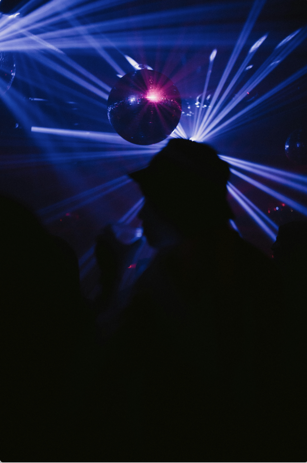 Silhouette of a person in a nightclub with disco ball and colorful laser lights.