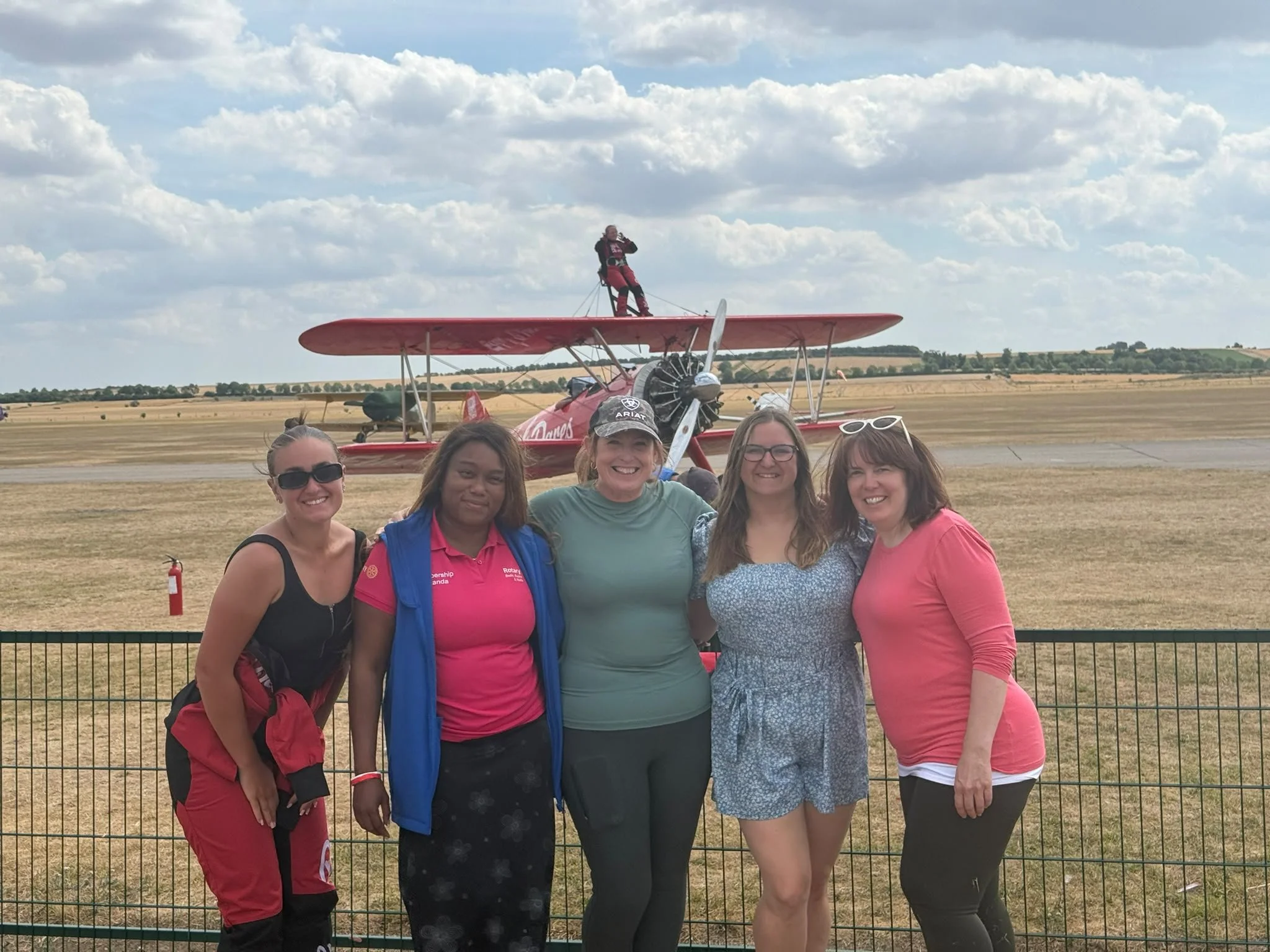 5 women standing in front of a plane with another standing on top of the wings