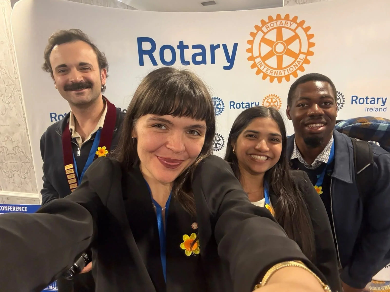 Four people taking a photo with the Rotary logo in the background
