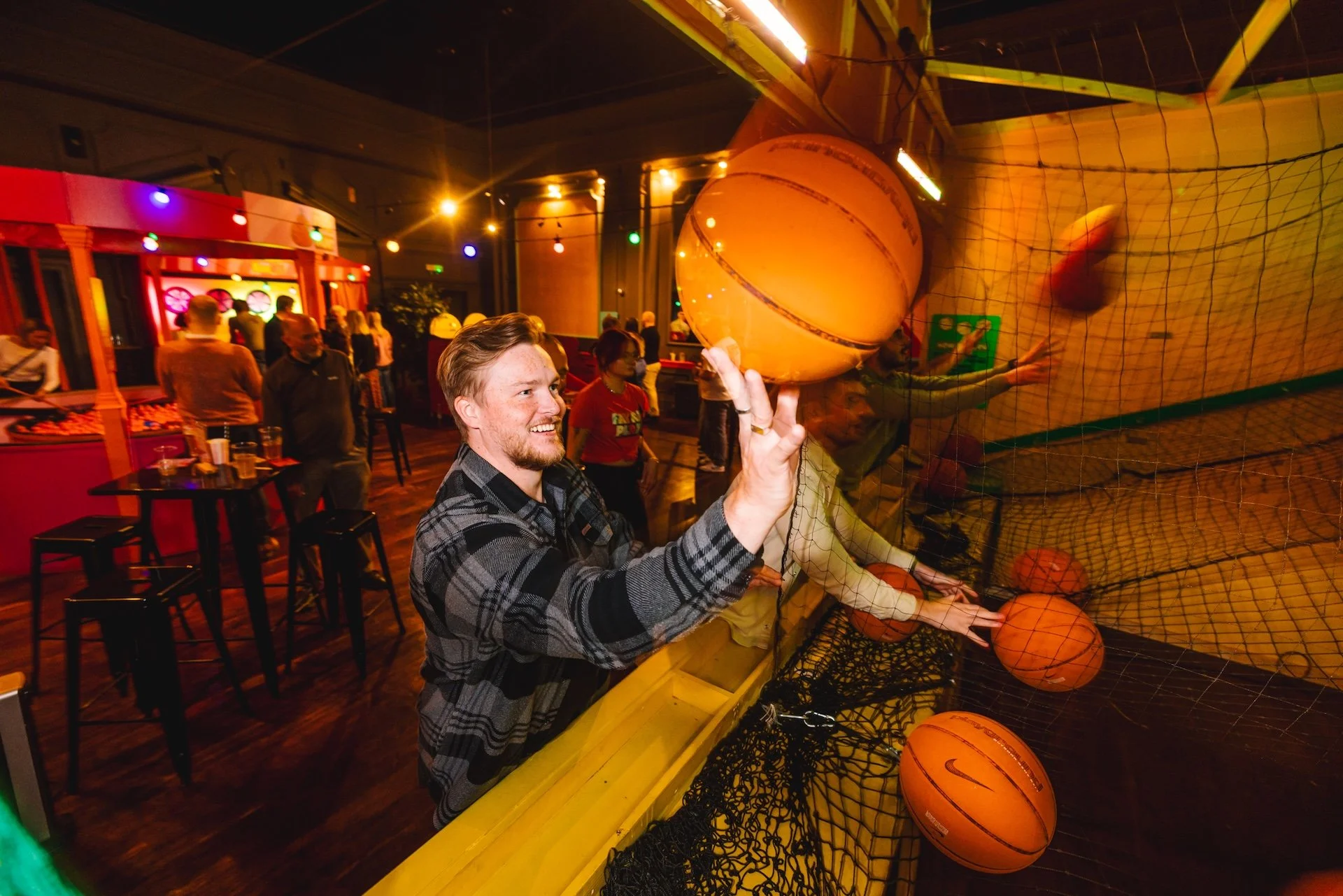 Man playing basketball arcade game at a bar or arcade, with other people in the background.