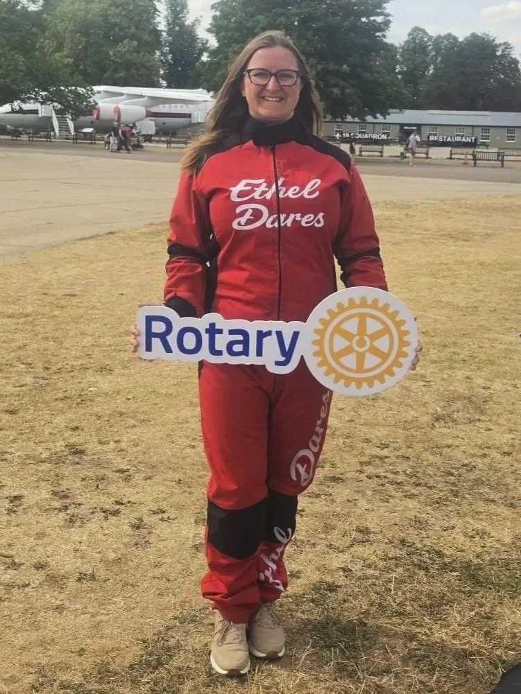 Woman in a red jump suit holding a sign that says Rotary