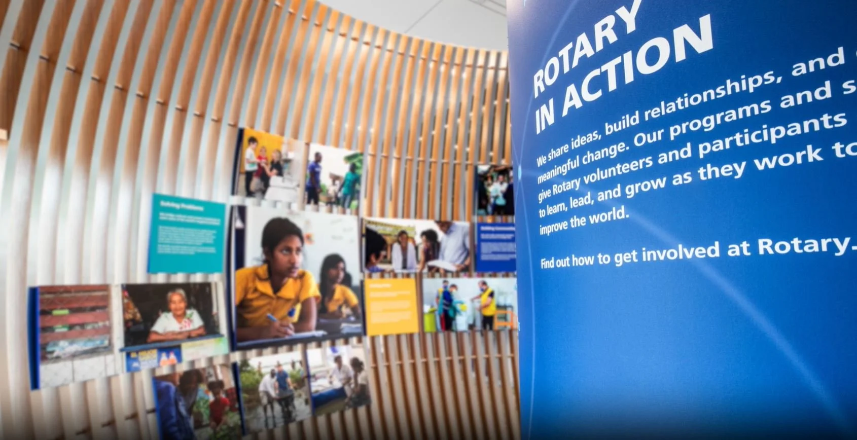 Exhibit display with the title 'Rotary in Action' and overview of Rotary Club activities, including photos of people engaging in community service and informational panels mounted on a wooden slat wall.