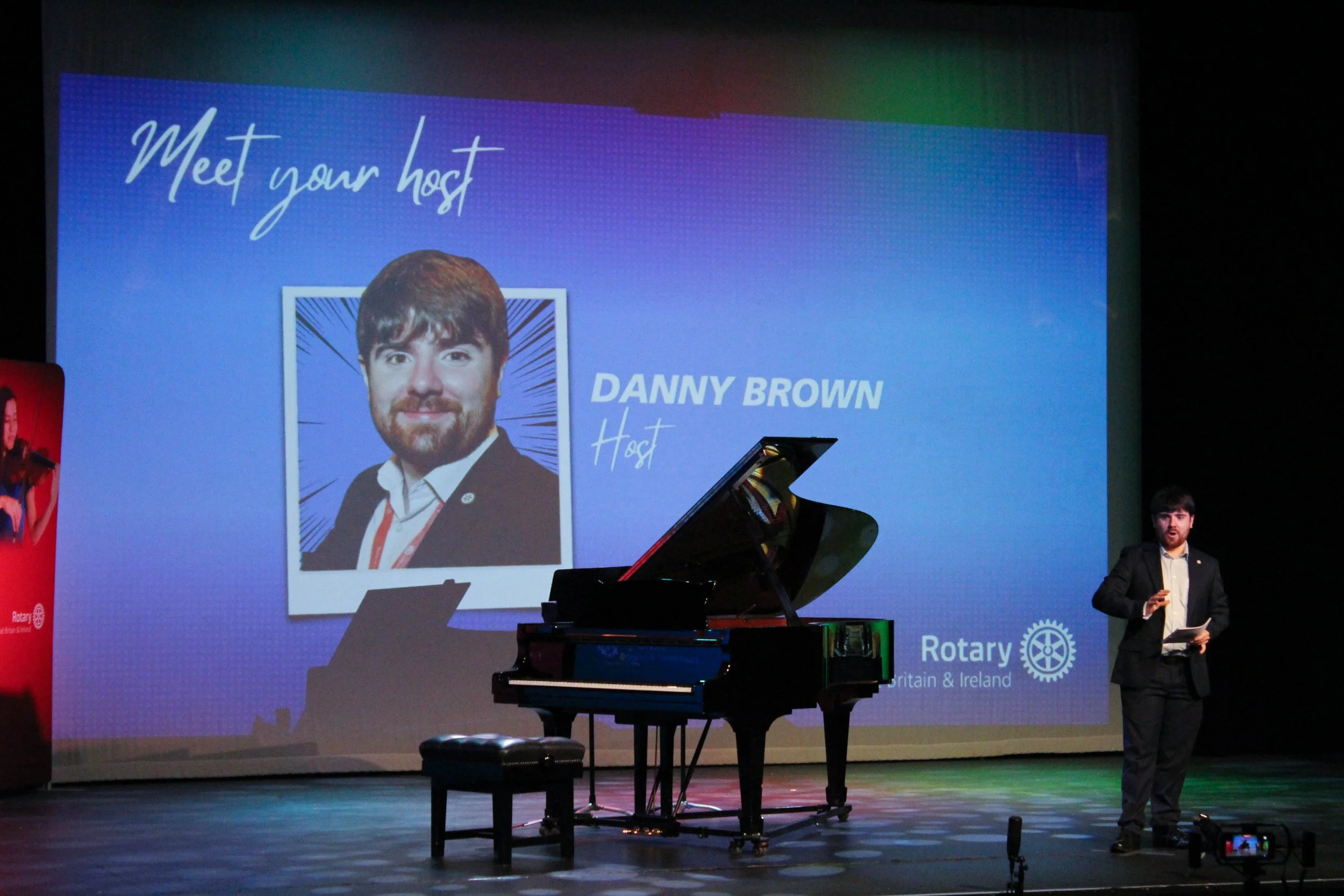 Danny on stage with a piano and a photo of himself on the screen