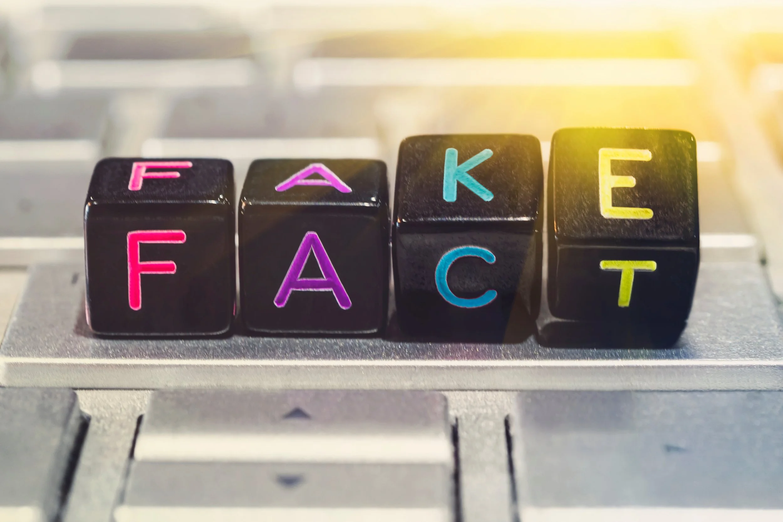 Black lettered dice on a computer keyboard spell “FAKE FACT,” symbolizing falsified child welfare case notes and record manipulation.