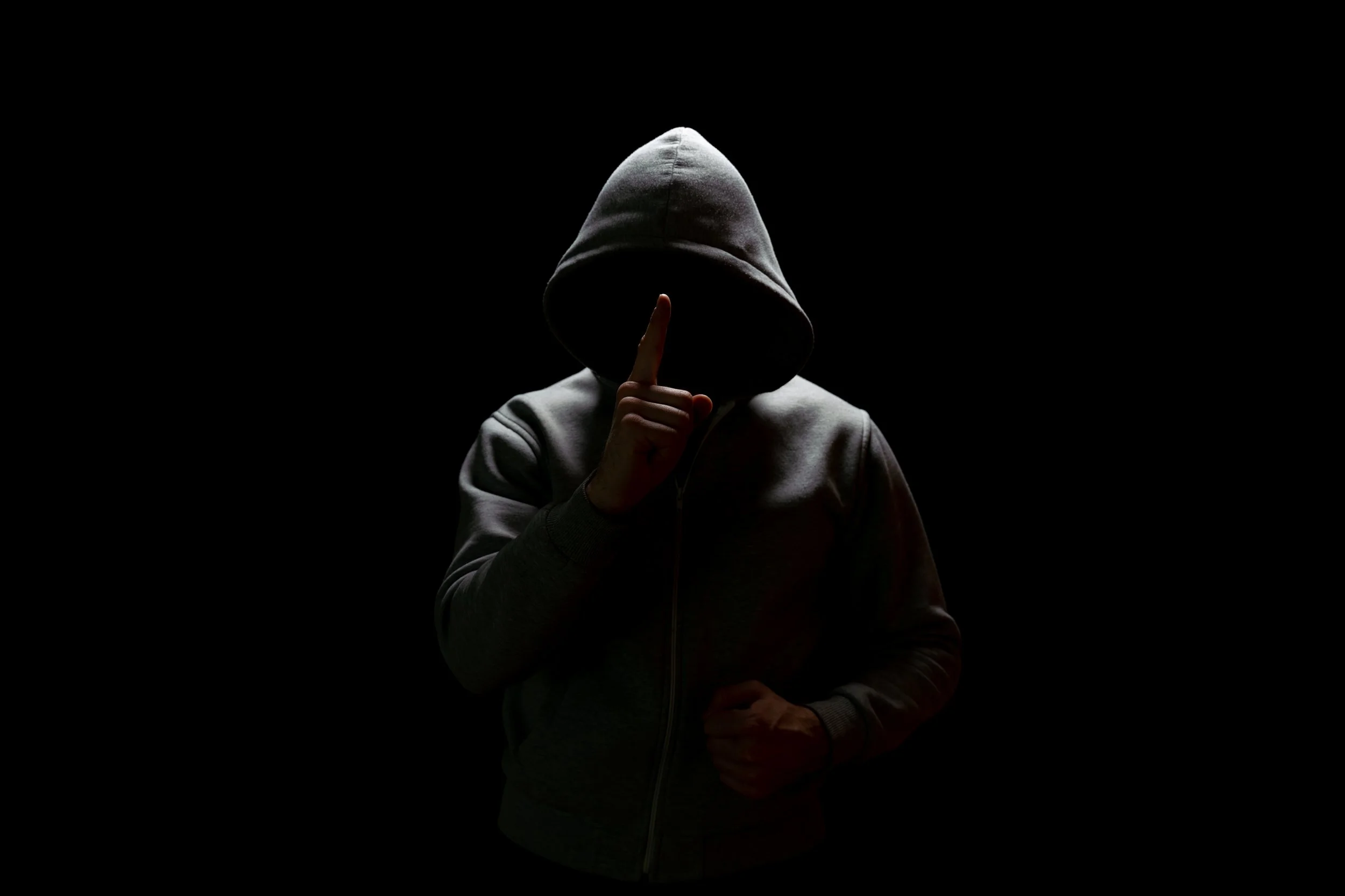 Hooded figure in shadow holding a finger to their lips, symbolizing an anonymous child welfare hotline report and the accountability gap it creates.