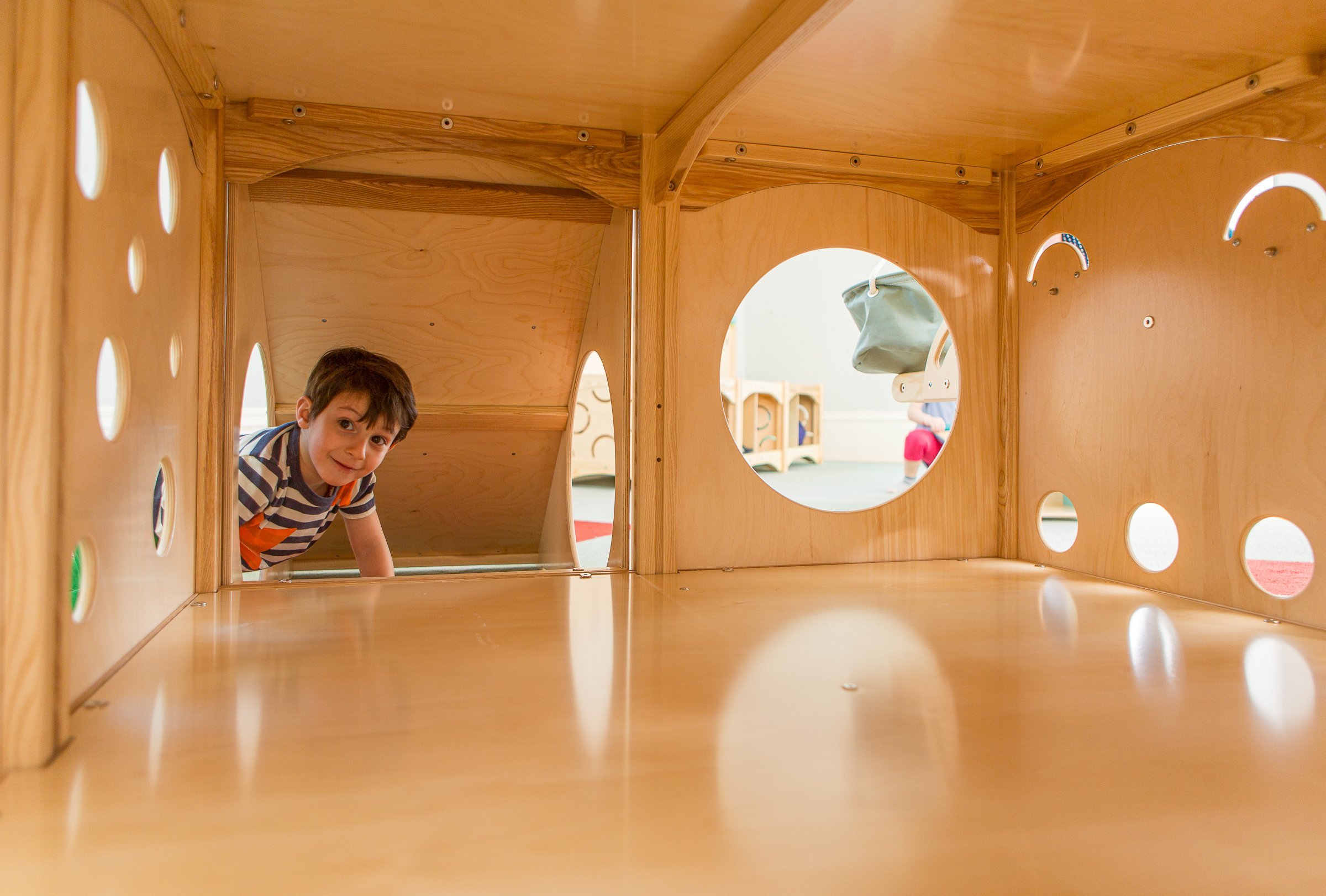 Young boy crawling through a wooden play structure with circular cutouts.