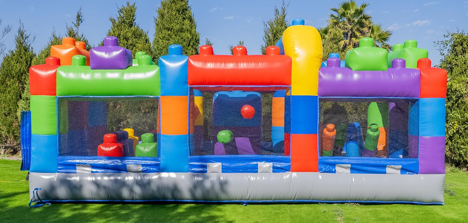 Colorful inflatable bounce house with mesh windows, set up outdoors on green grass with trees and blue sky in the background