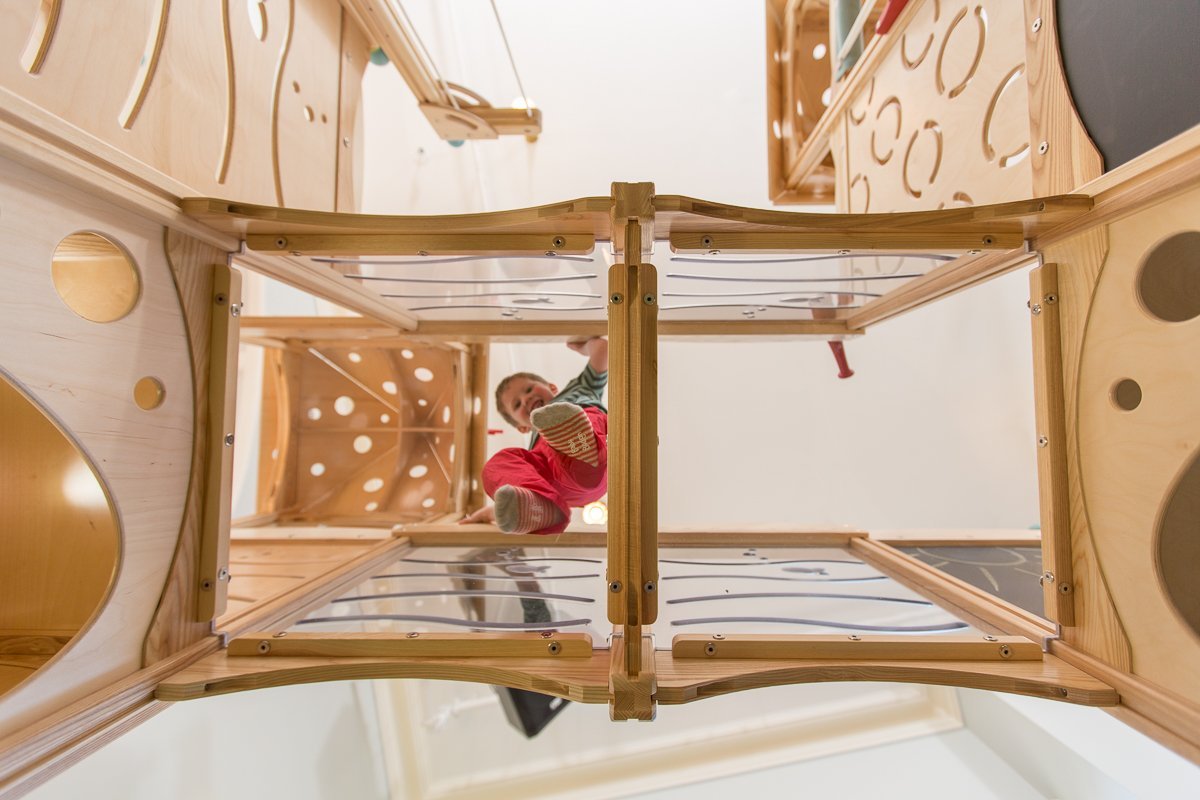 Child playing inside a wooden multi-story playground structure with circular cutouts.