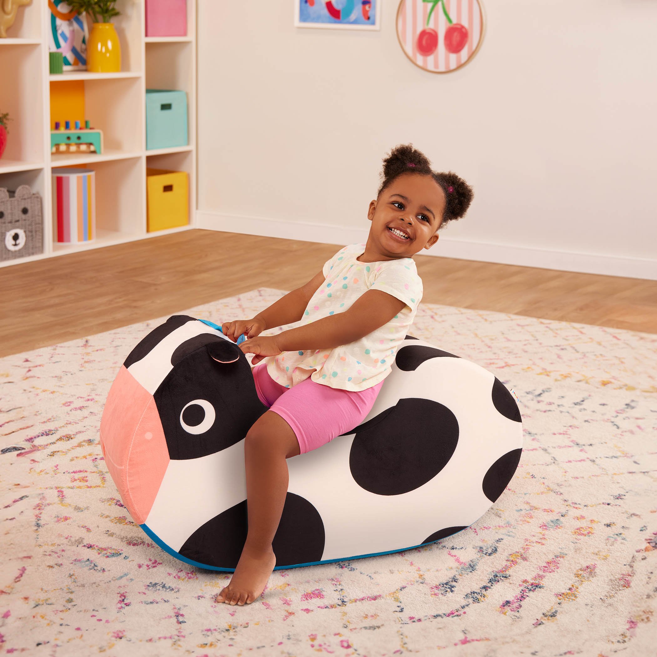 A young girl sitting on a cow-shaped-shaped toy in a colorful playroom.