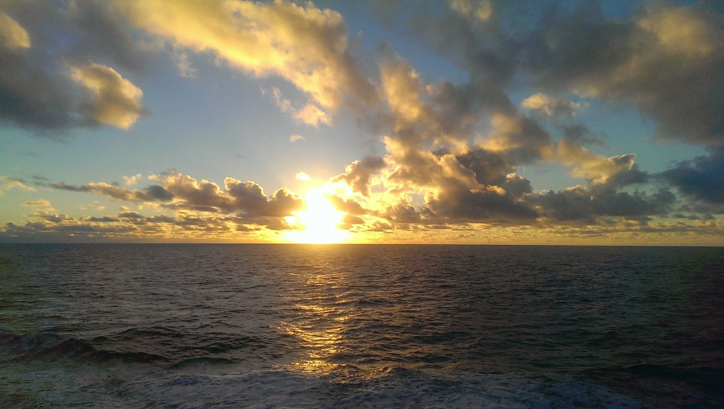 Sunset over the ocean with clouds in the sky.