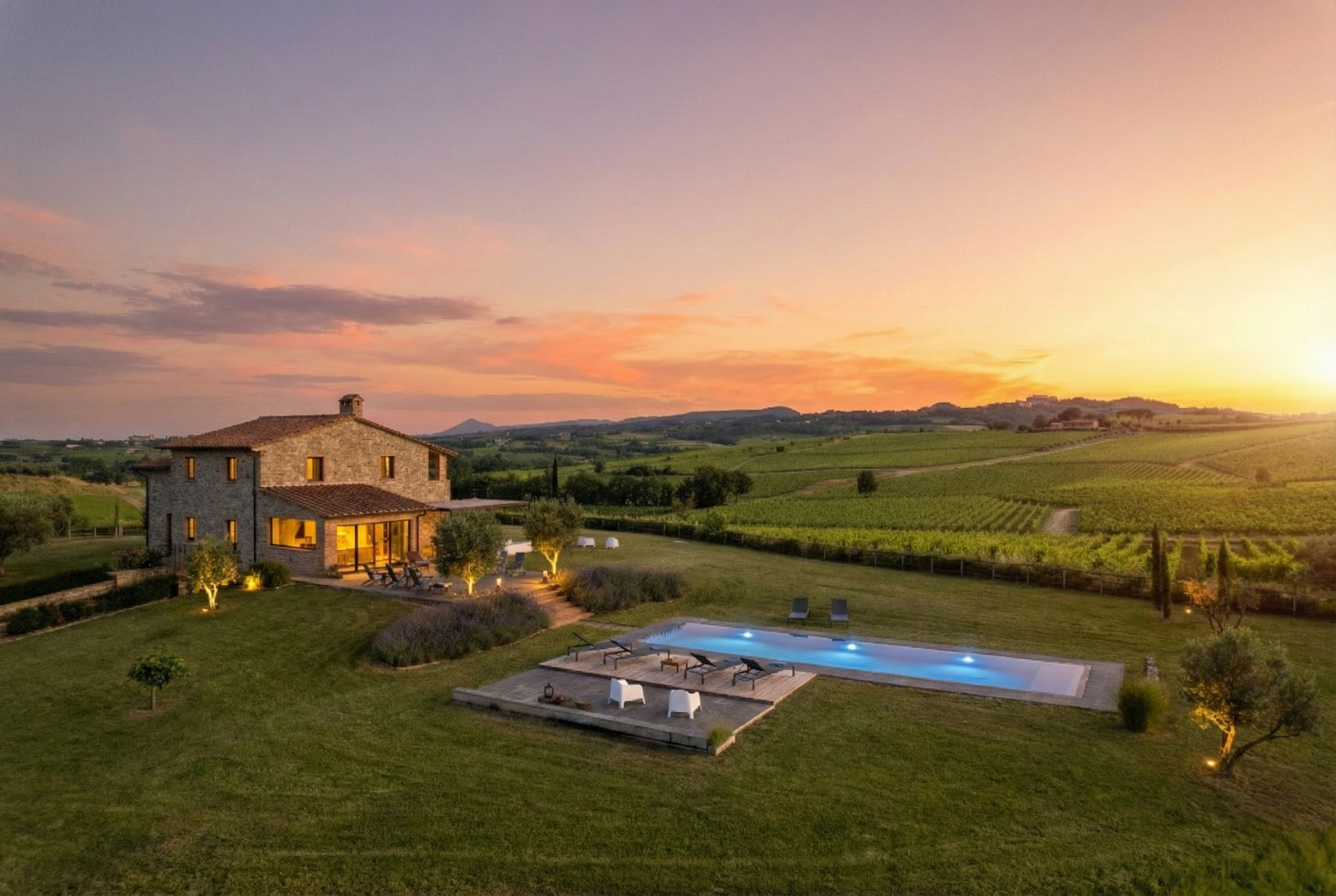 A scenic view of a countryside house with a swimming pool at sunset, surrounded by green fields and rolling hills.