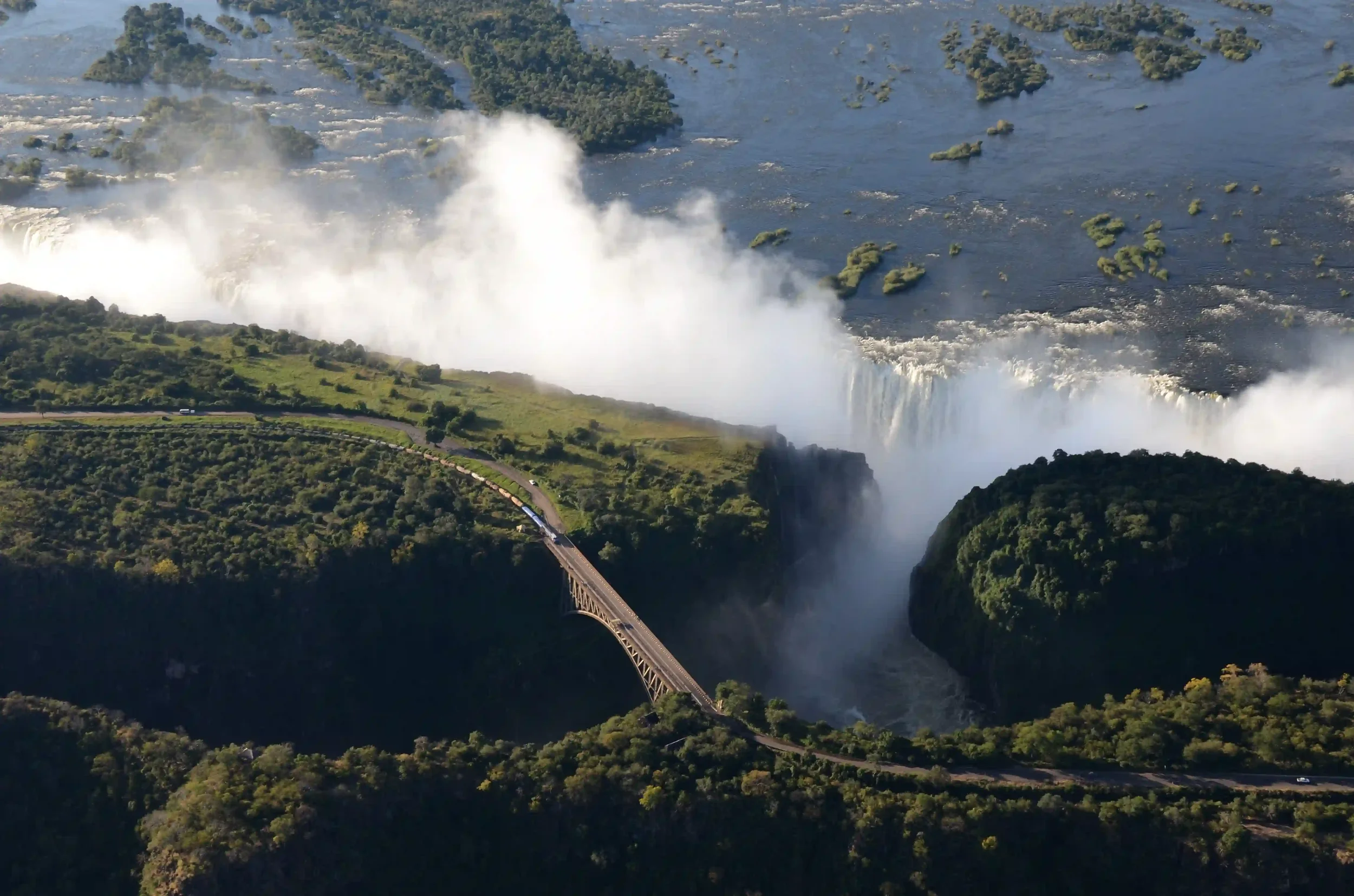 Aerial view of victoria falls with water crashing over the edge, lush green landscape and a bridge